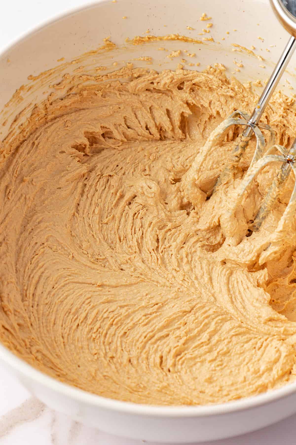 peanut butter oatmeal cookie dough in a large white bowl with an electric mixer