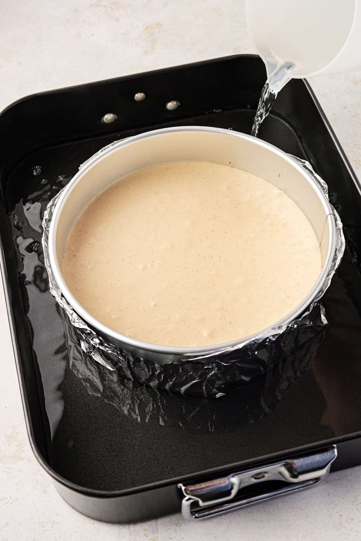 cheesecake batter in a springform pan surrounded by water in a larger baking dish