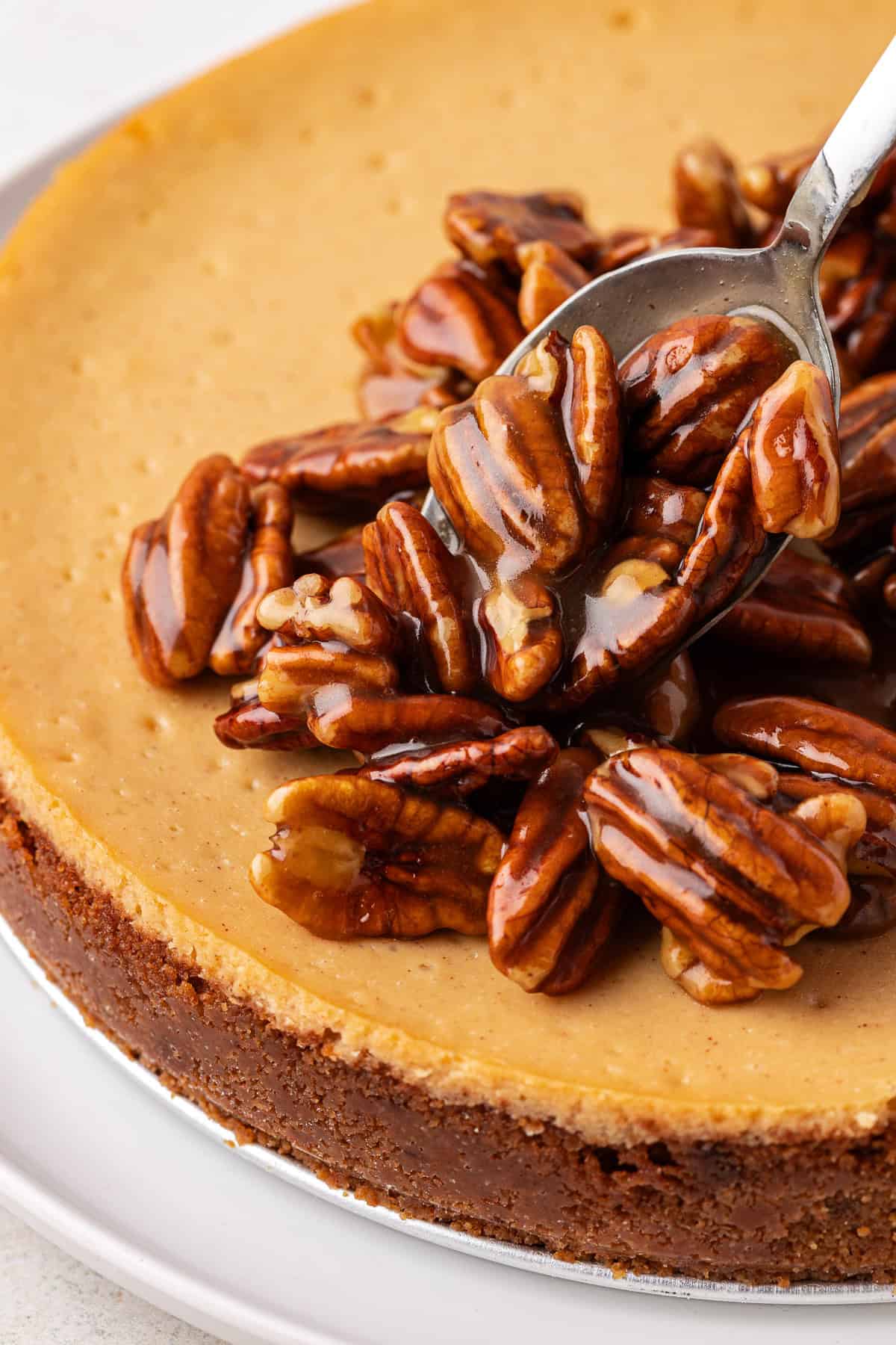 pecan pie filling being spooned on top of a cheesecake