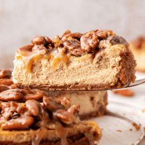 side view of a slice of pecan pie cheesecake being lifted away from the rest of the cheesecake