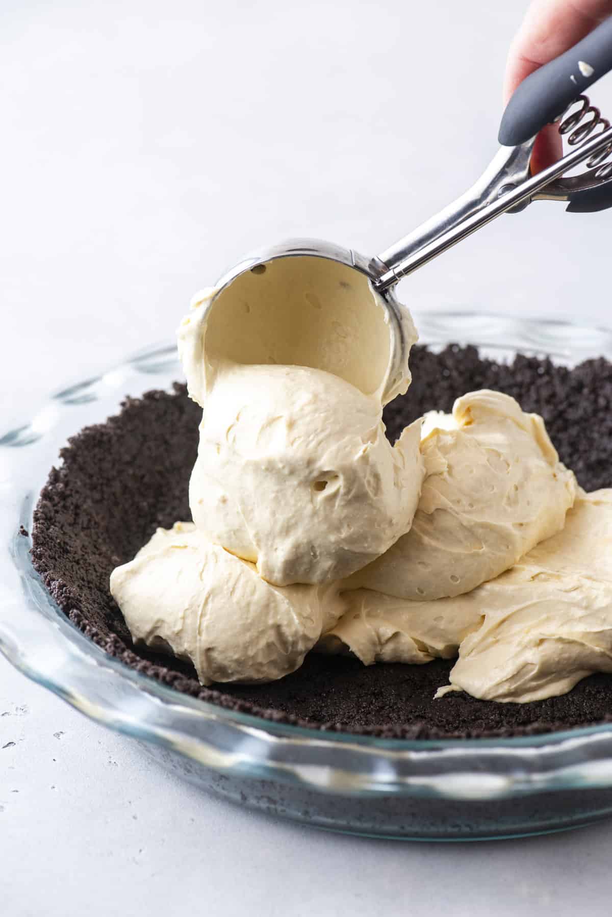 oreo crust in a glass pie dish with creamy caramel filling being scooped on top