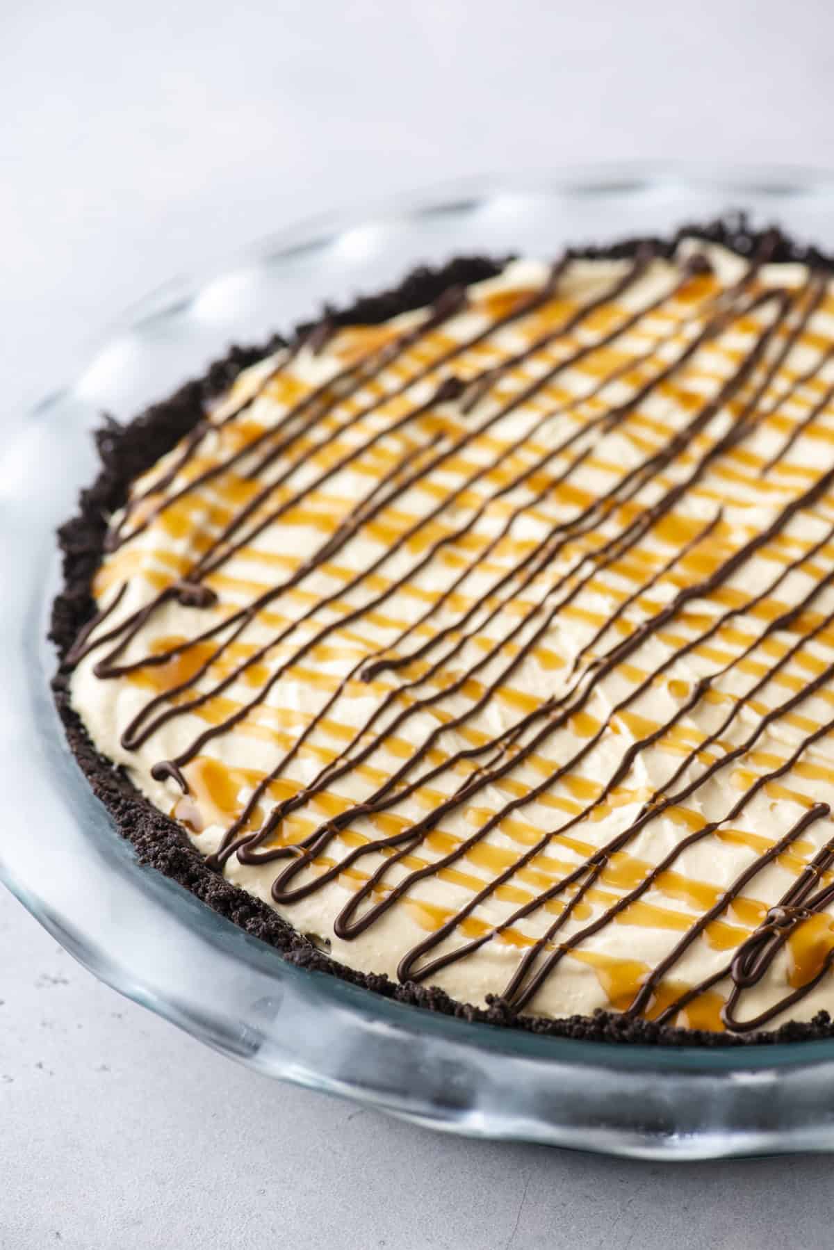 turtle pie topped with chocolate and caramel drizzles in a clear pie dish