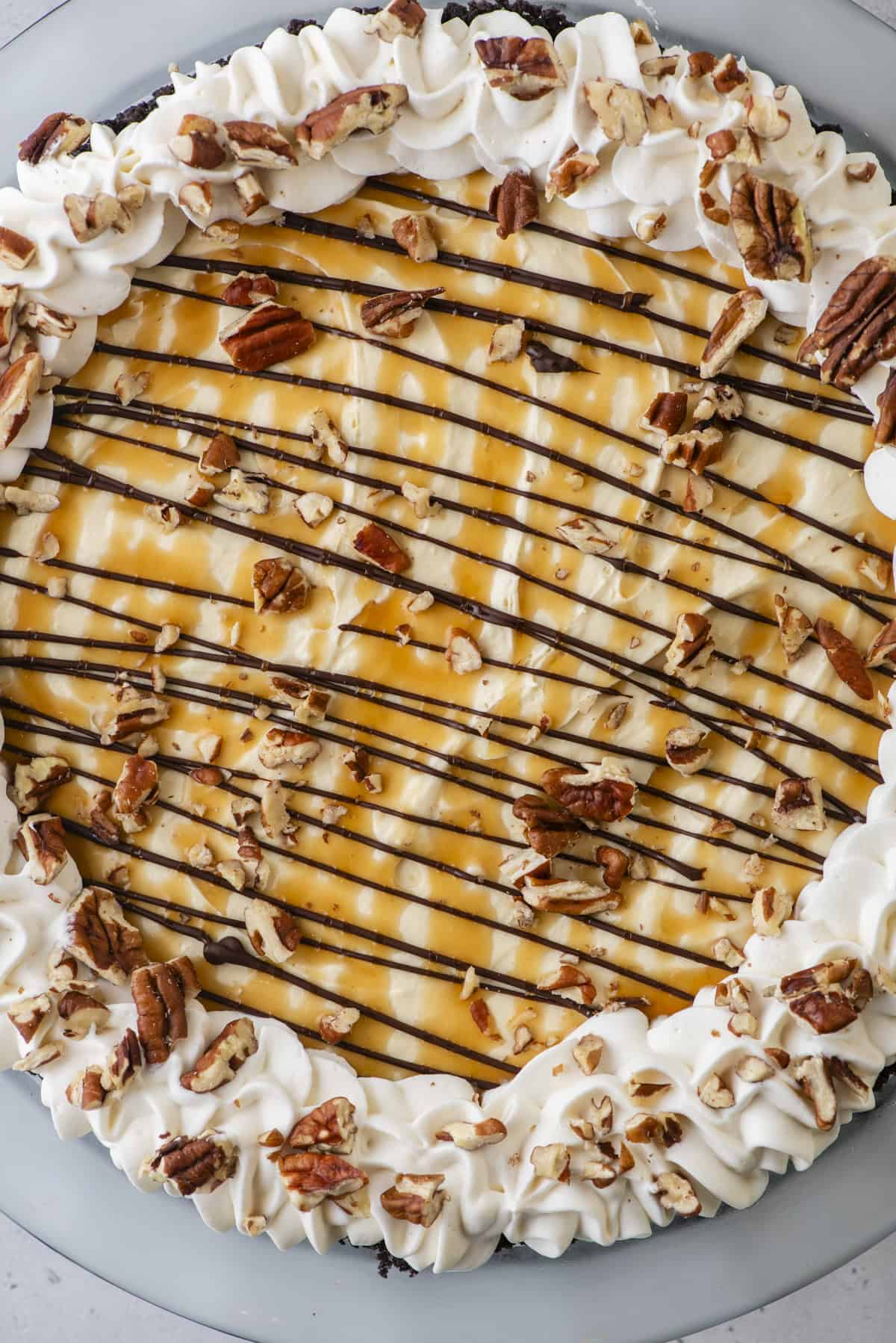 over head view of a turtle pie topped with whipped cream, chocolate, caramel and pecans