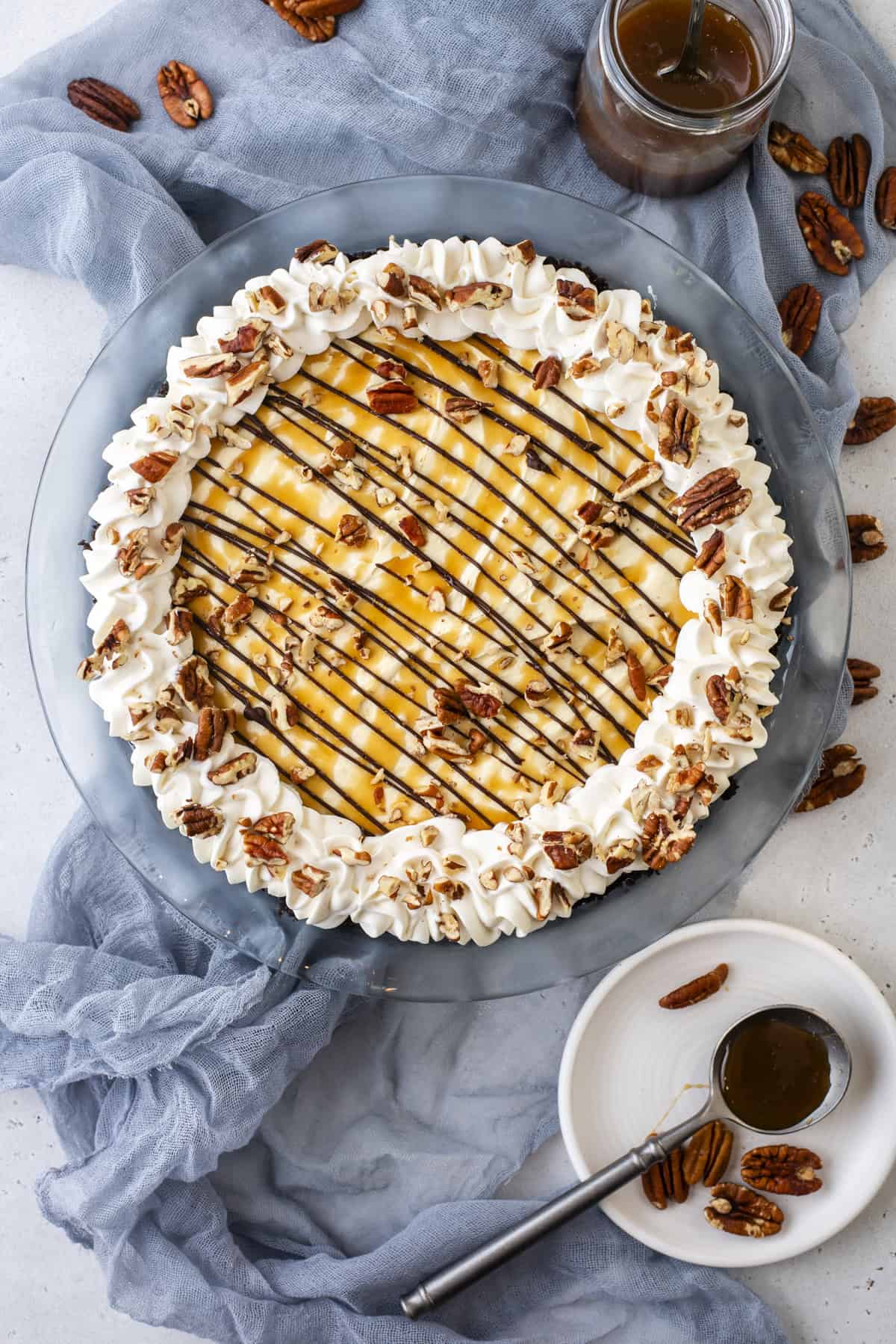 over head view of a turtle pie topped with caramel, chocolate, whipped cream, and pecans surrounded by pecans and caramel sauce