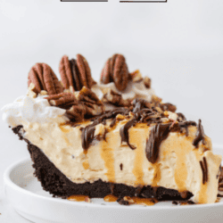 a slice of turtle pie topped with pecans, chocolate and caramel drizzles on a small white plate with pecan pieces scattered around