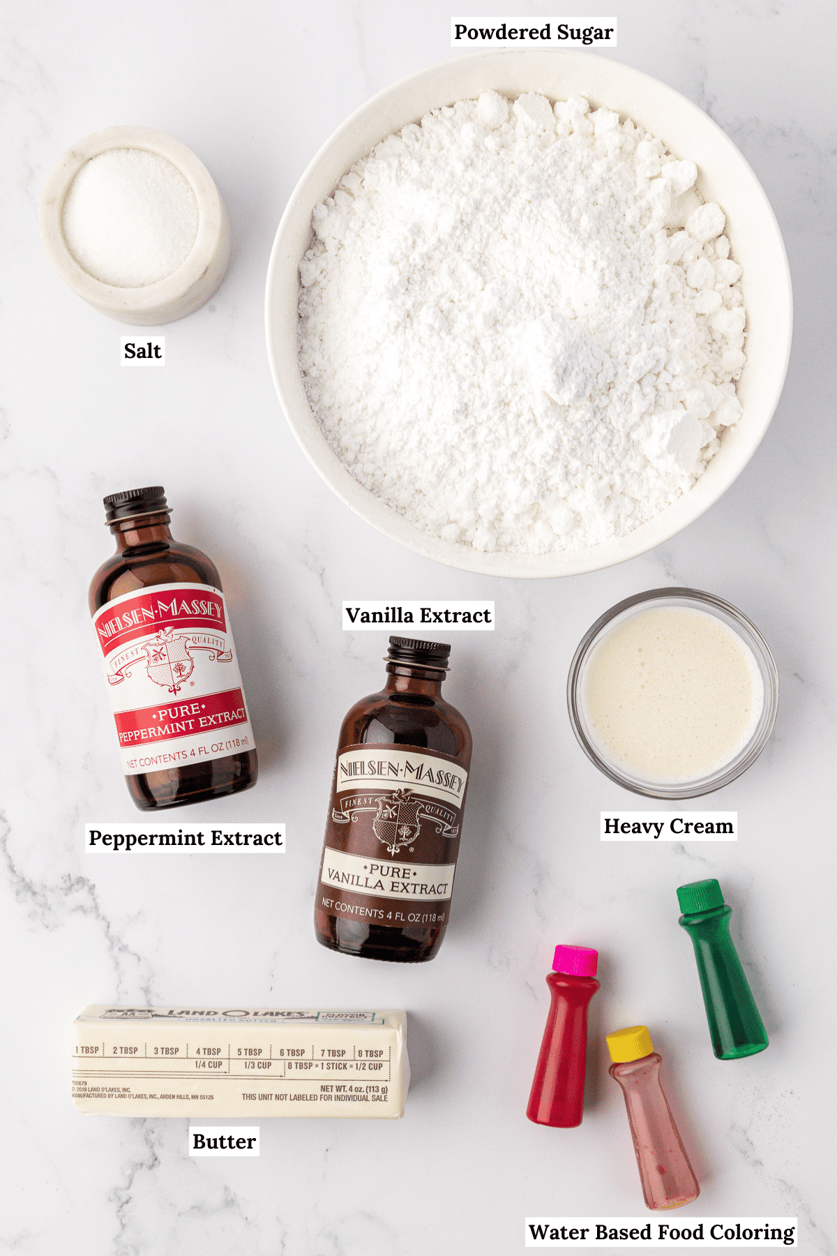 overhead view of ingredients for butter mints including powdered sugar, salt, peppermint extract, vanilla extract, heavy cream, butter and water based food coloring