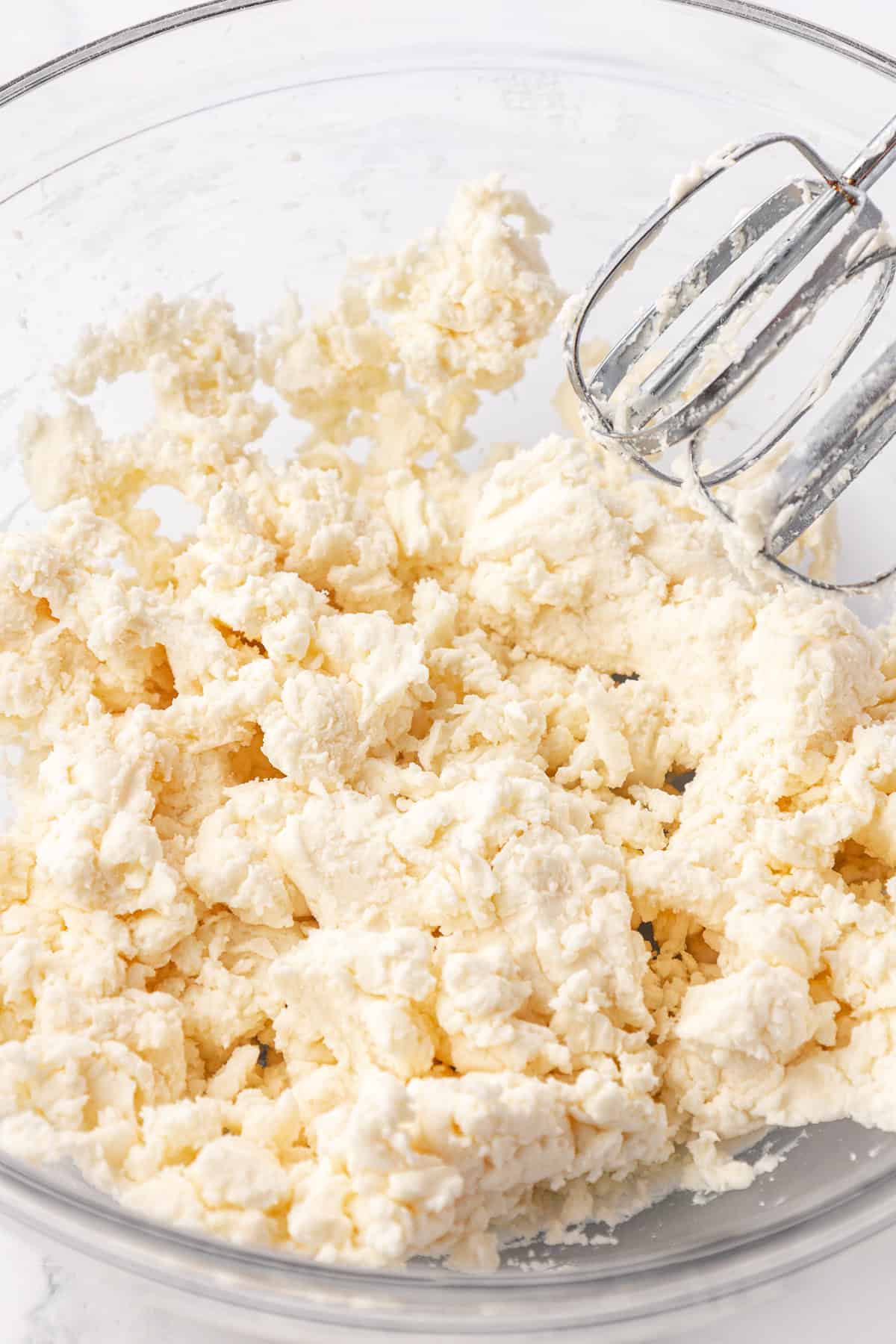 dough for butter mints in a clear glass bowl with mixer tools leaning on the side