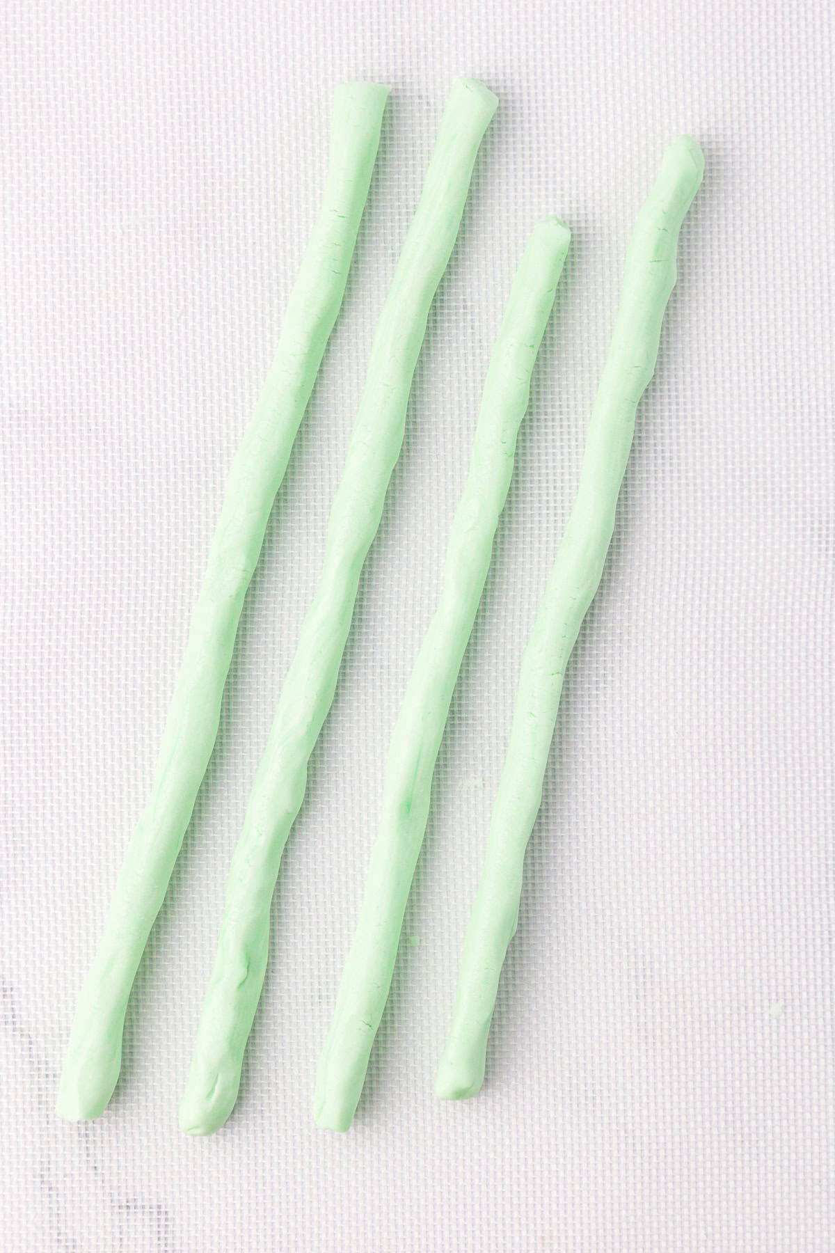 4 light green ropes of butter mints not yet cut, laying on a white silicone mat