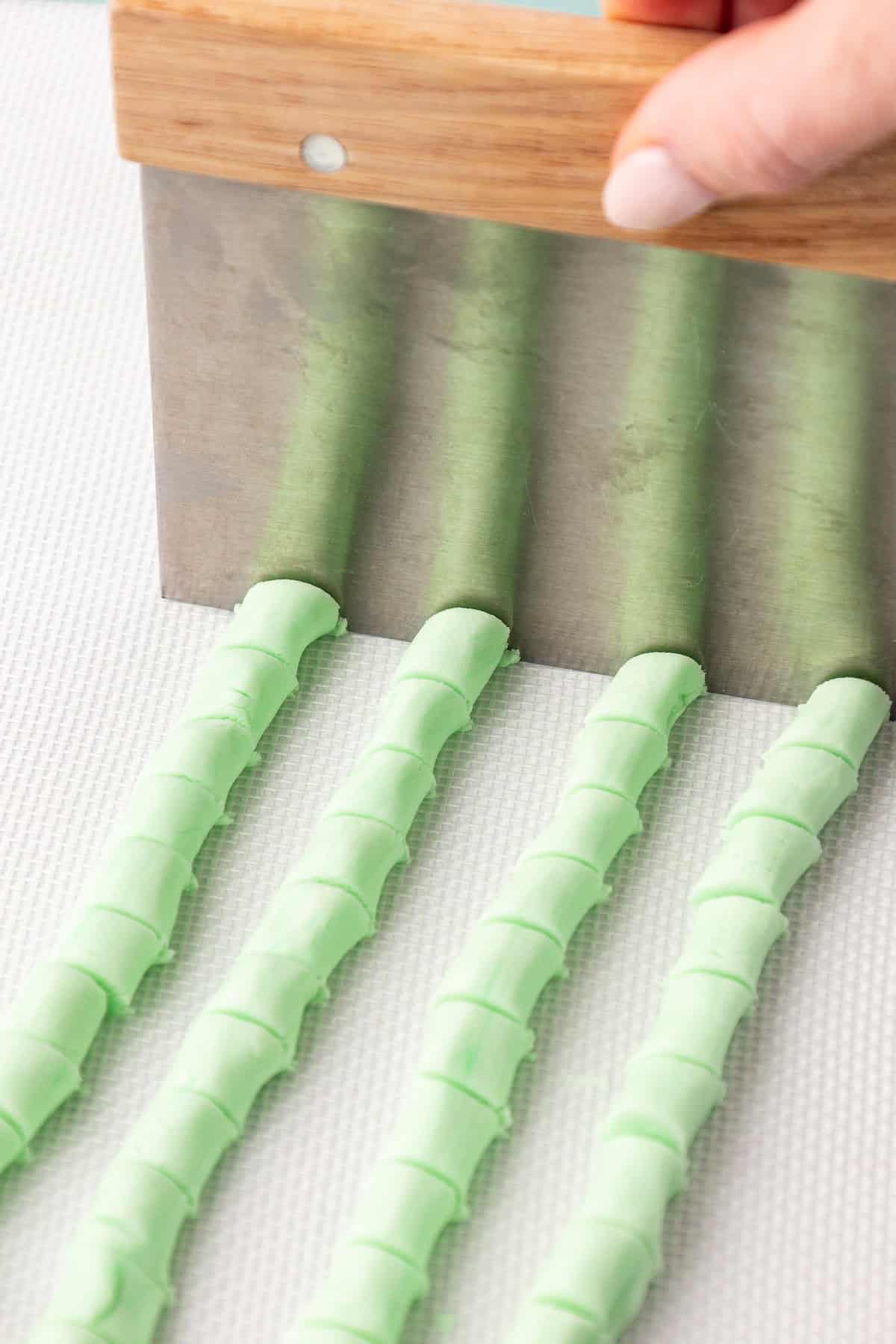 four rows of green butter mint rope being cut into small pieces