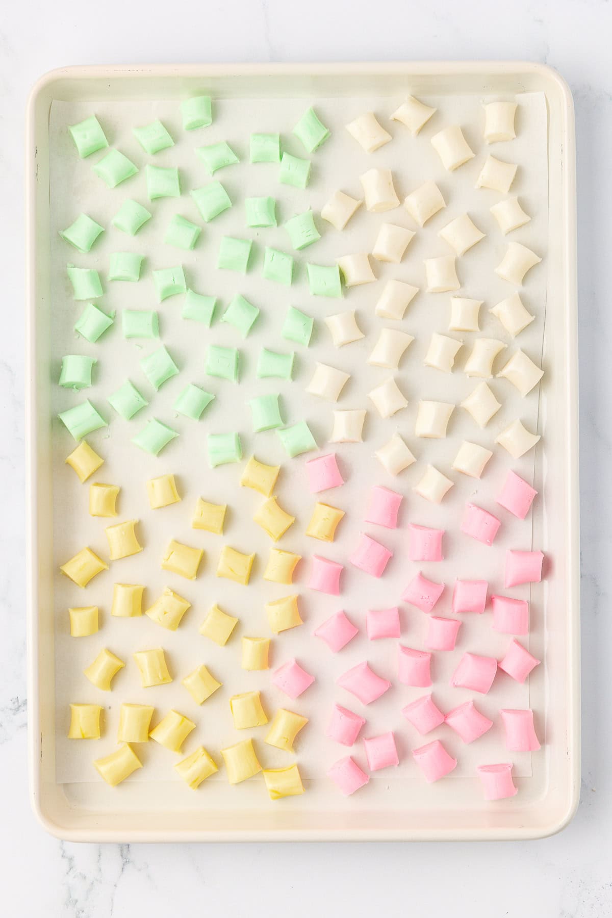 over head view of a sheet pan with spread out green, white, yellow, and pink butter mints drying on it