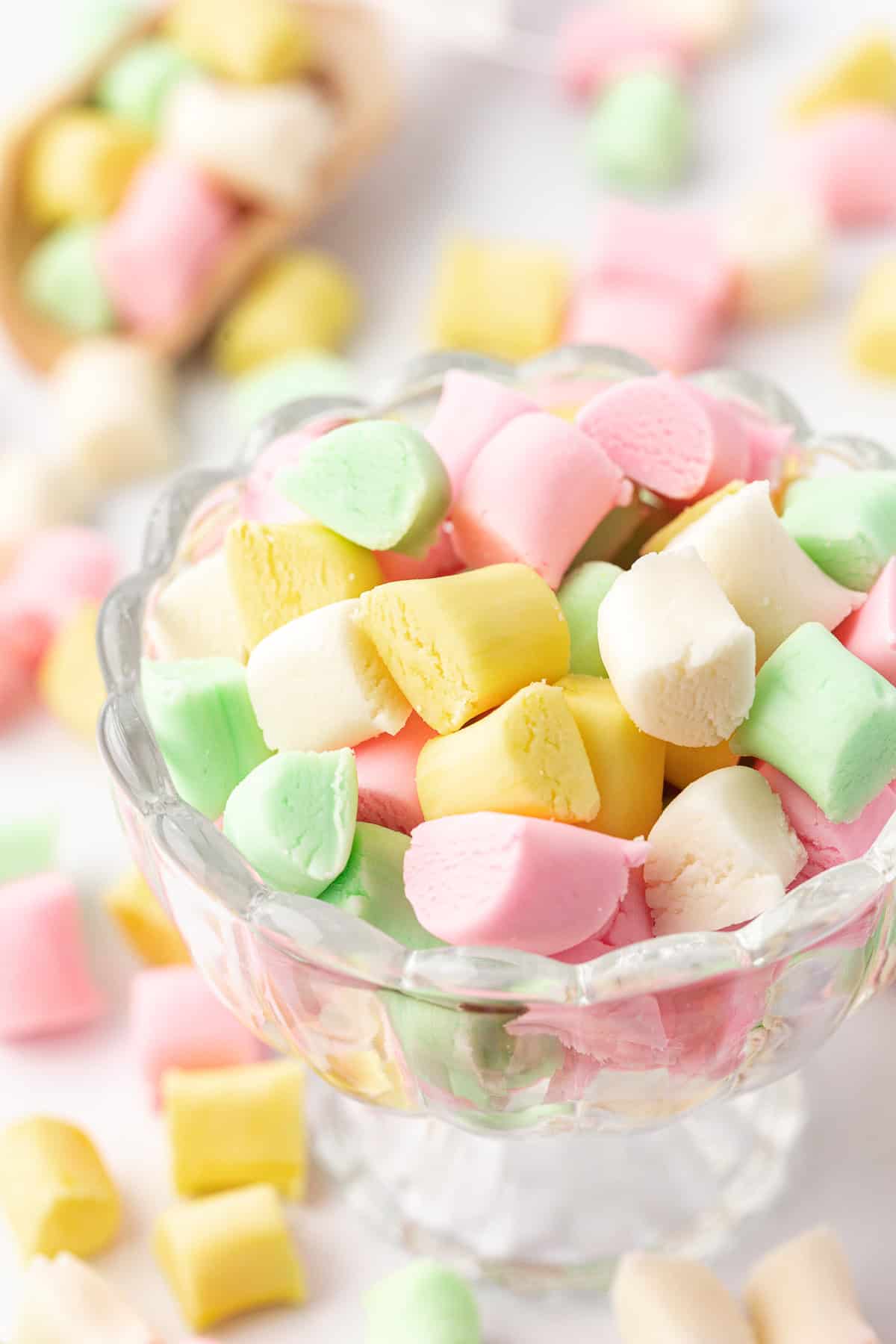 small glass trifle dish full of pink, yellow, white and green butter mints with more mints scattered around