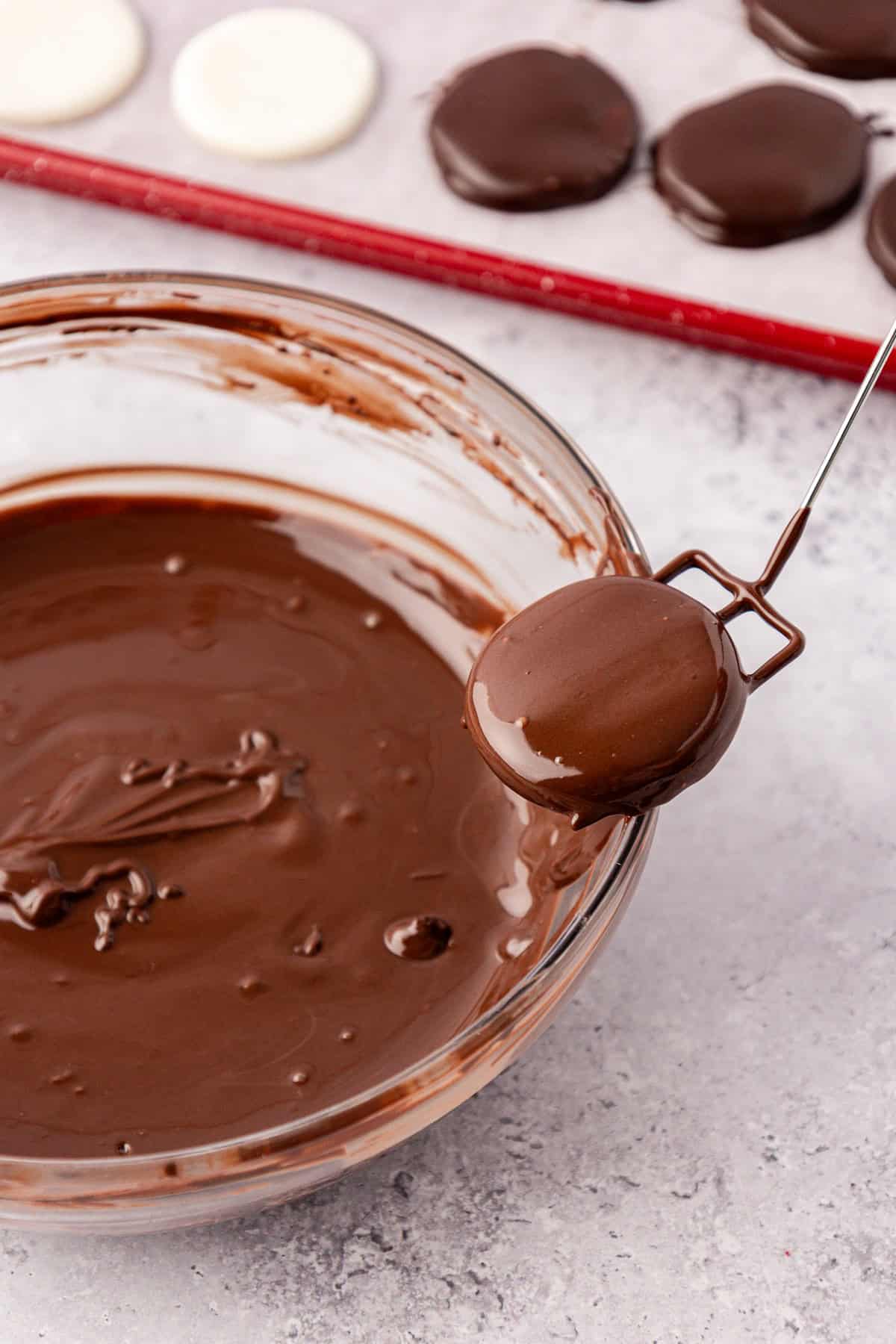 a peppermint patty that was just dipped into a clear glass bowl of melted chocolate being lifted out by the edge of the bowl