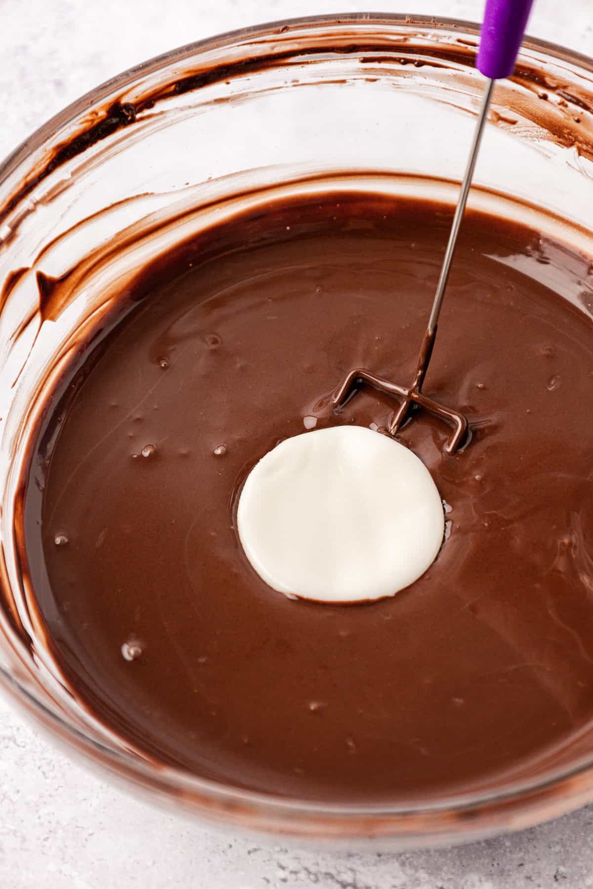 a white disc of peppermint patty filling being dipped into a clear glass bowl full of melted chocolate