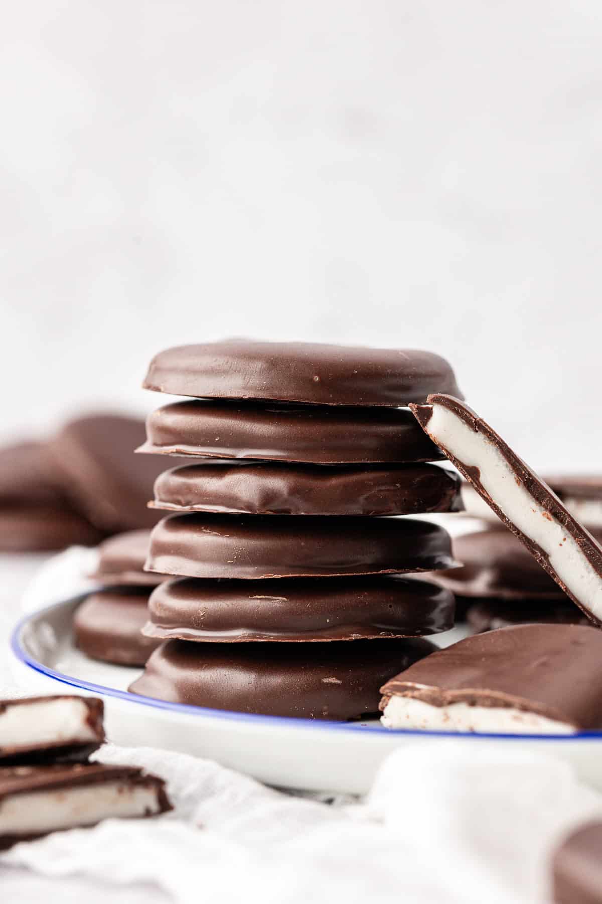 a stack of peppermint patties on a plate surrounded by more patties, cut in halves