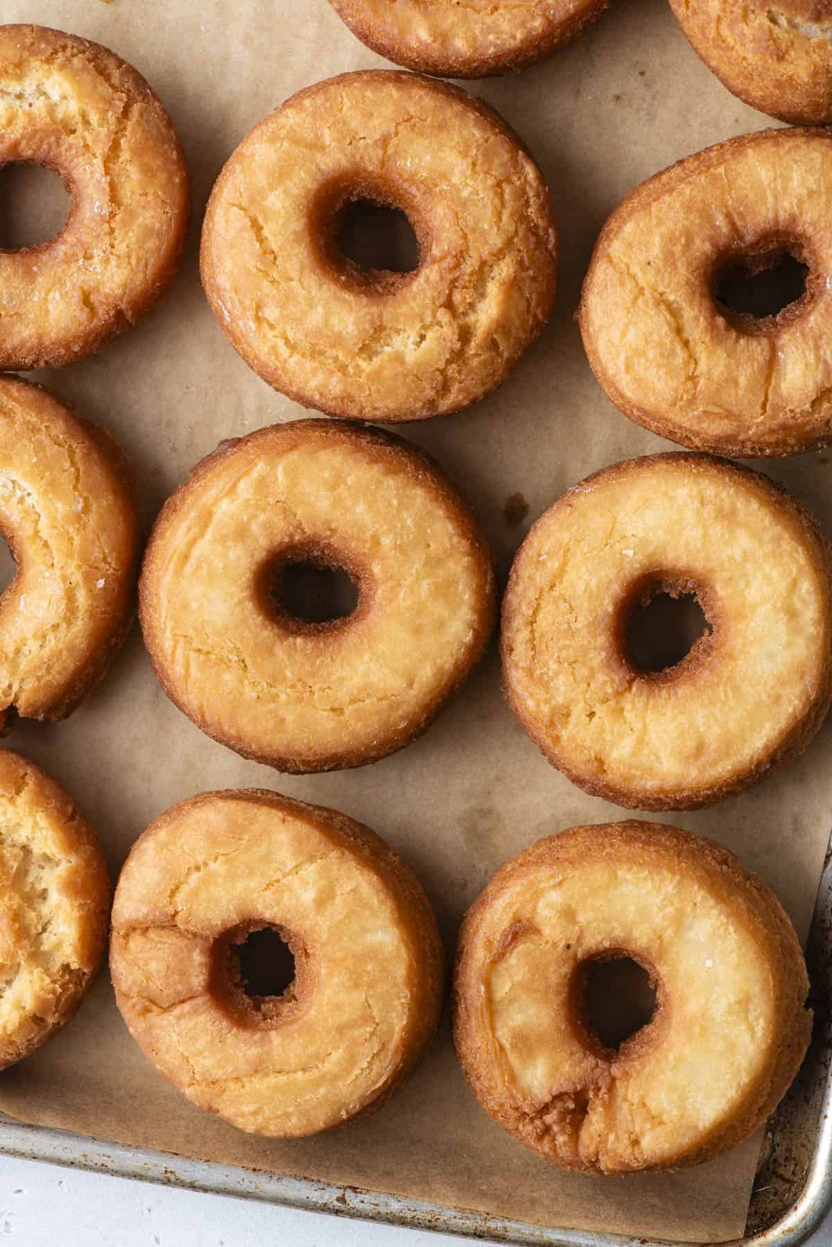 close up of cake donuts on a baking sheet lined with brown parchment paper