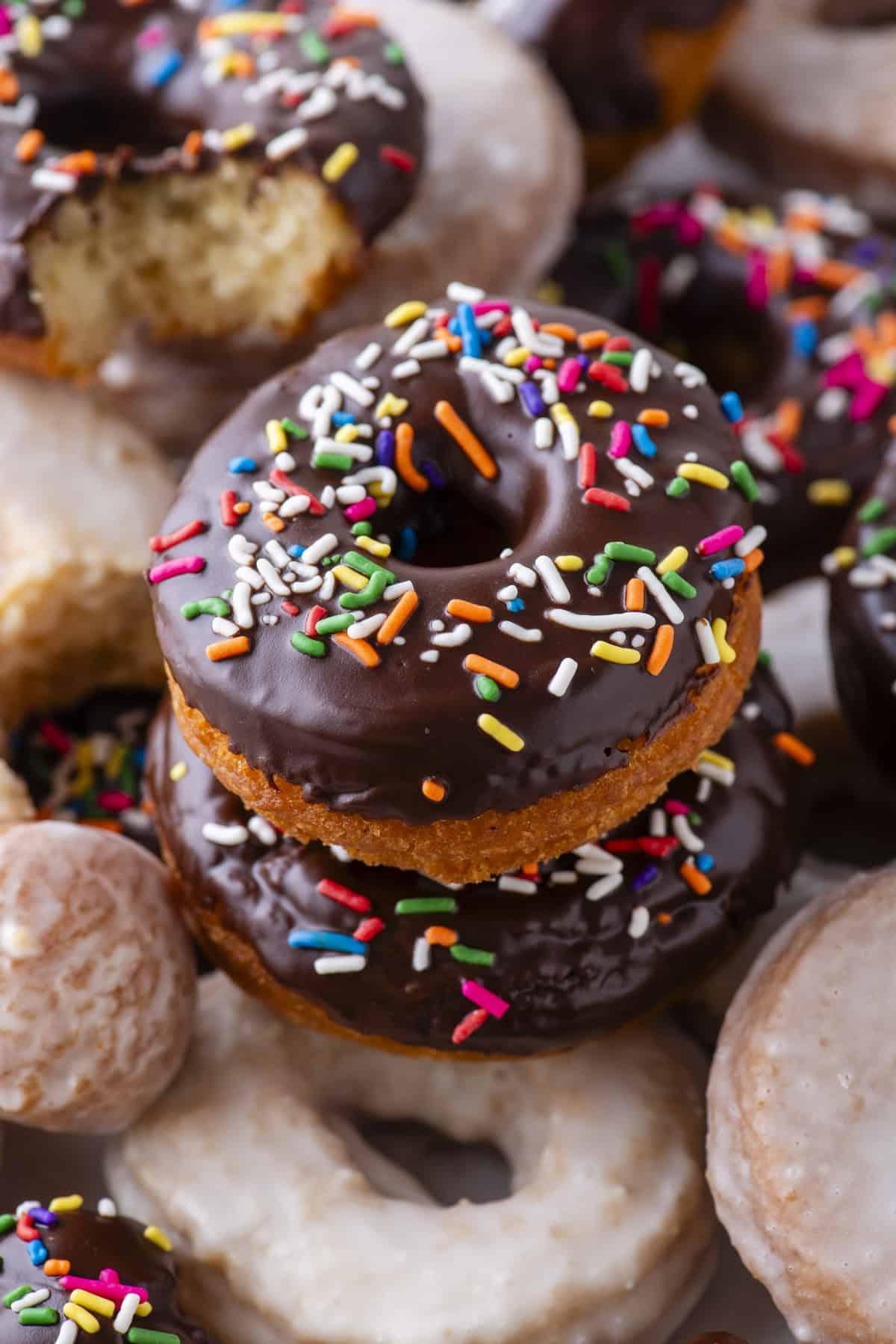 a mix of simple glazed and chocolate glazed with sprinkle donuts stacked on top of and around each other