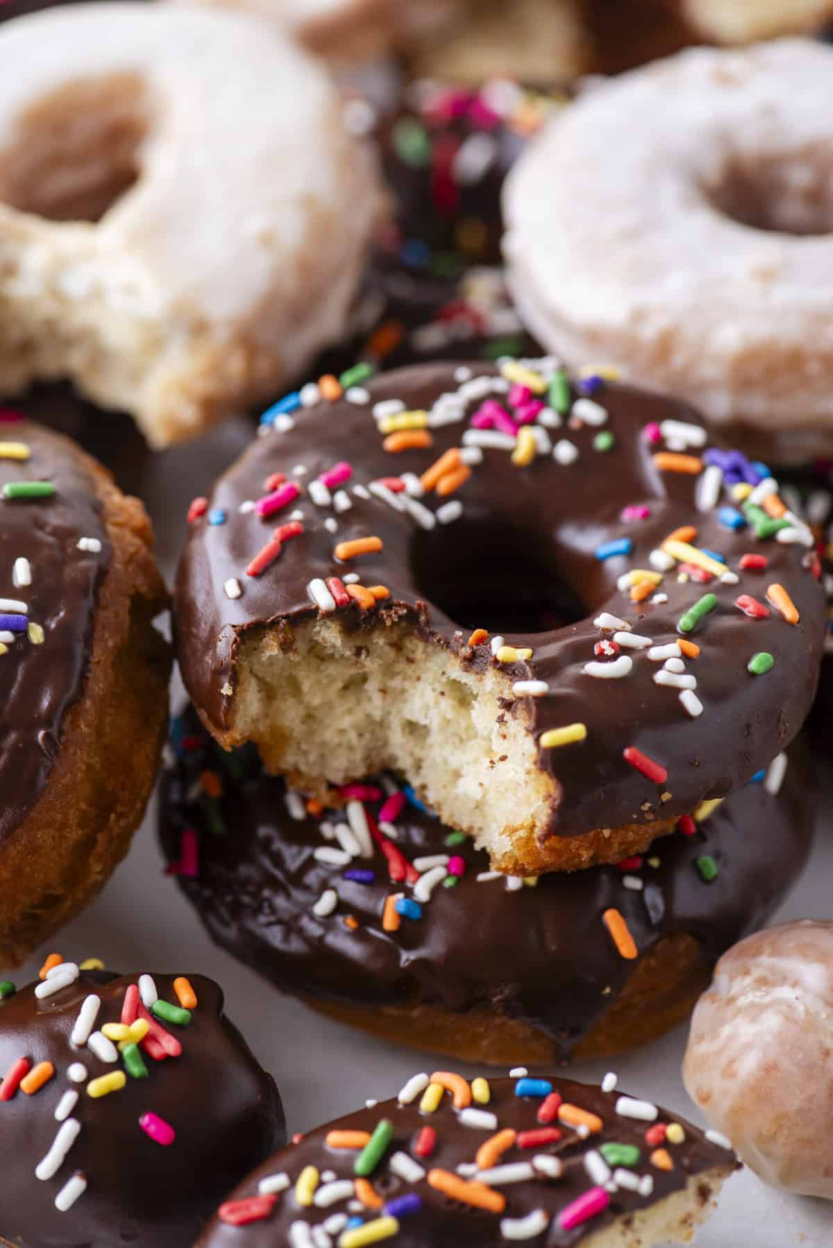 close up of cake donuts glazed with chocolate and topped with sprinkles, and more that are just glazed