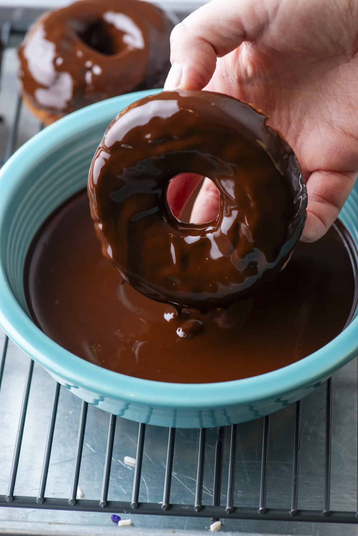 a cake donut being dipped in a bowl of chocolate glaze