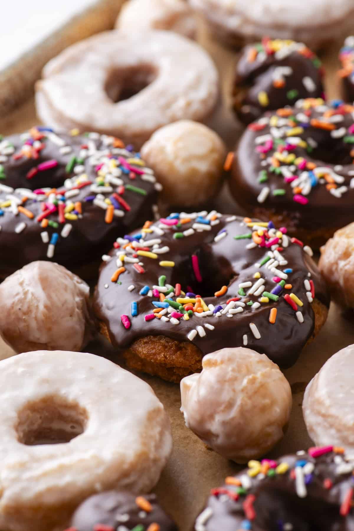 close up of scattered cake donuts, a mix of donut holes, regular glazed donuts and chocolate glazed with sprinkles