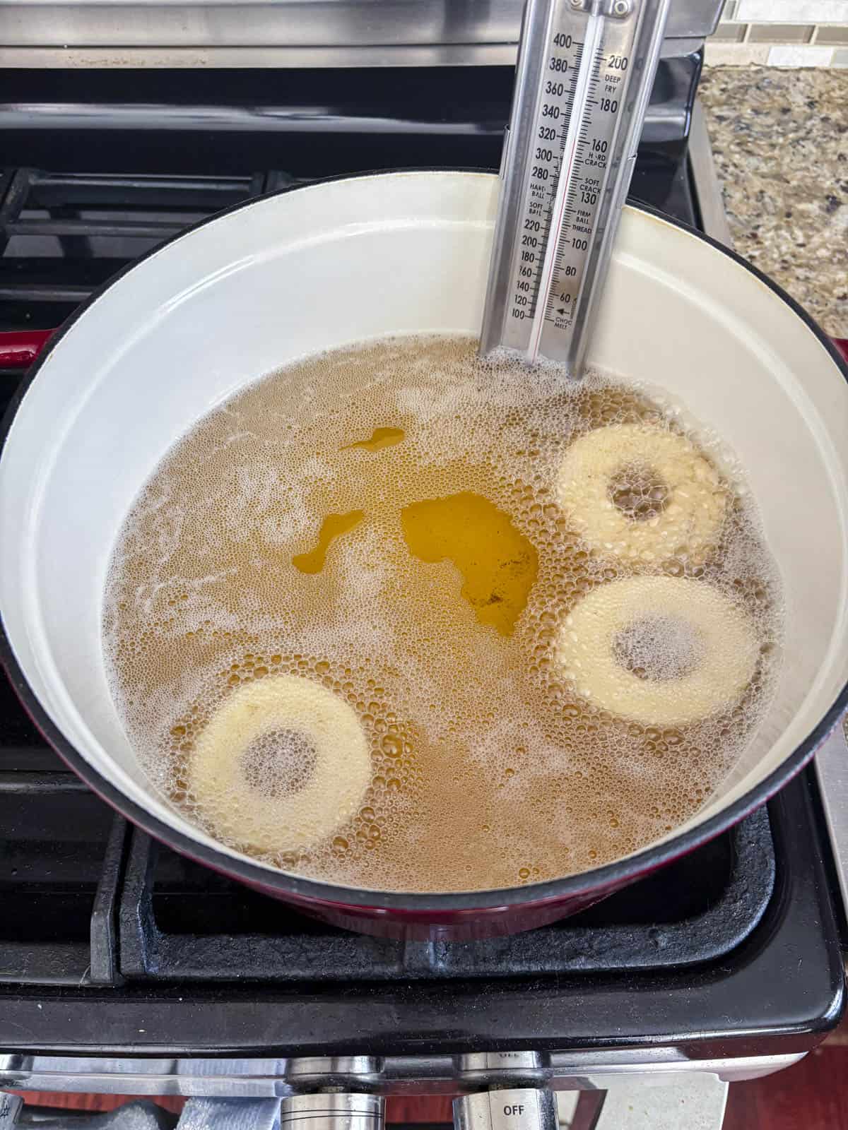 three donuts frying in a hot pot of oil with a thermometer attached to the side of the pot