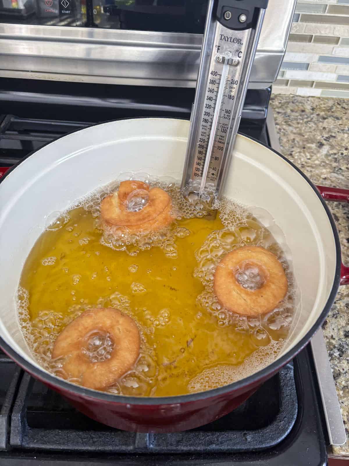 three donuts frying in a pot with a thermometer on the side of it