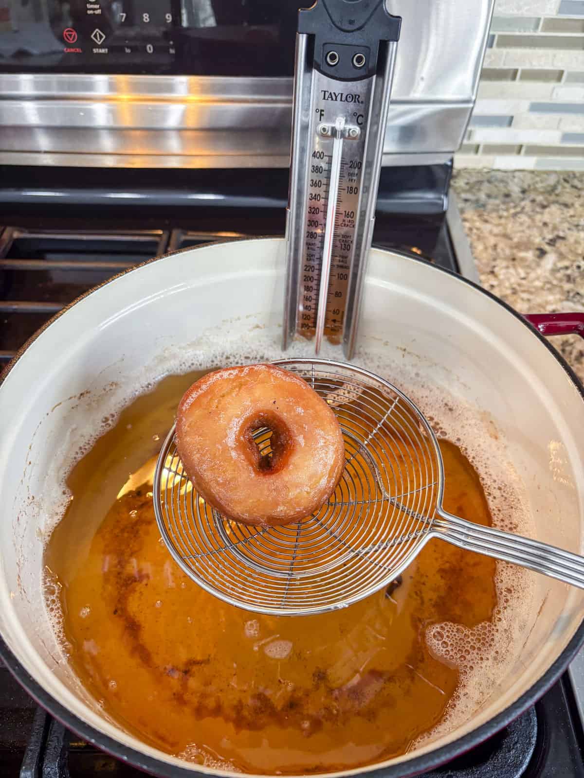 a donut being lifted out of a pot full of oil with a thermometer on the side of it