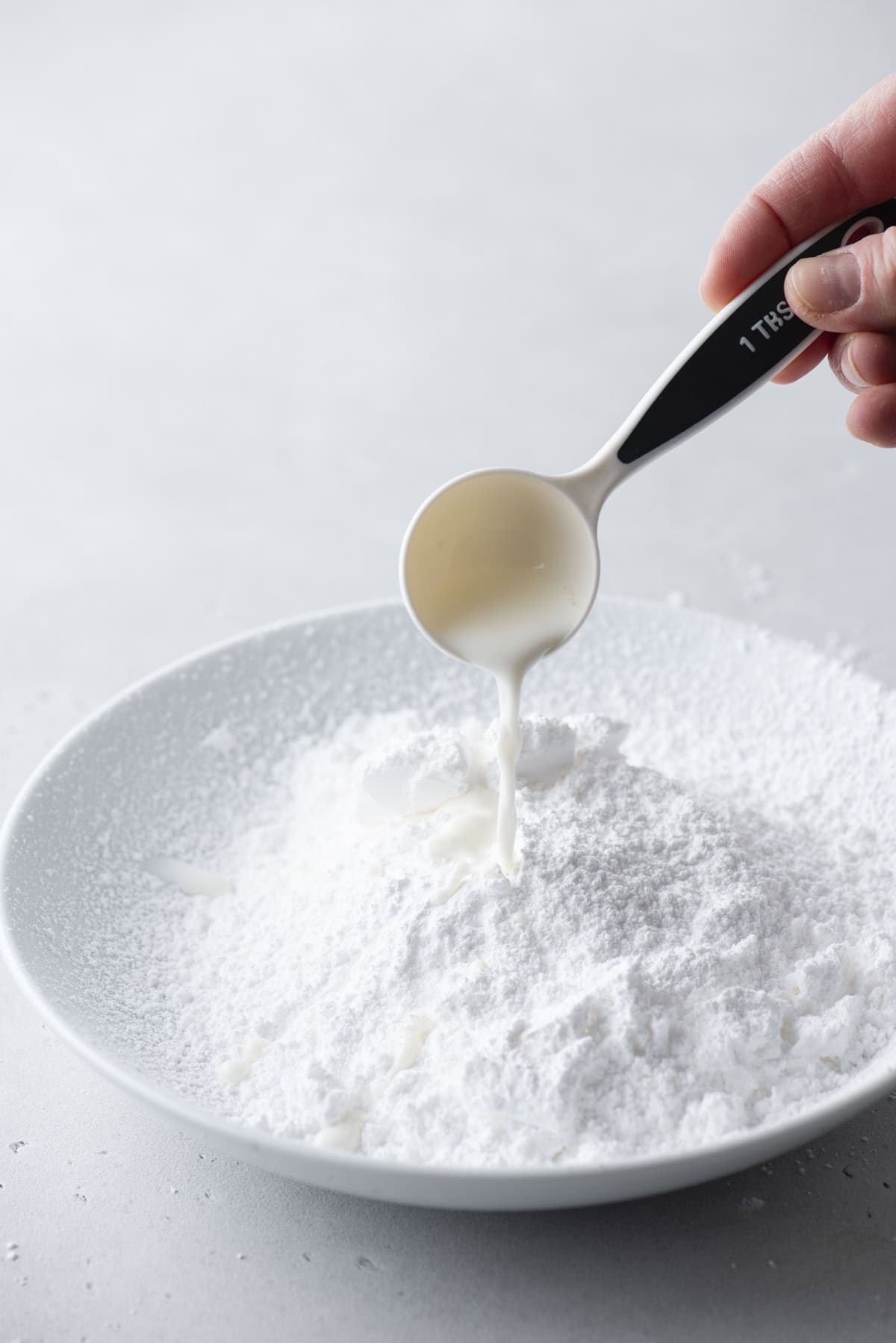 a bowl of powdered sugar with milk being poured into it