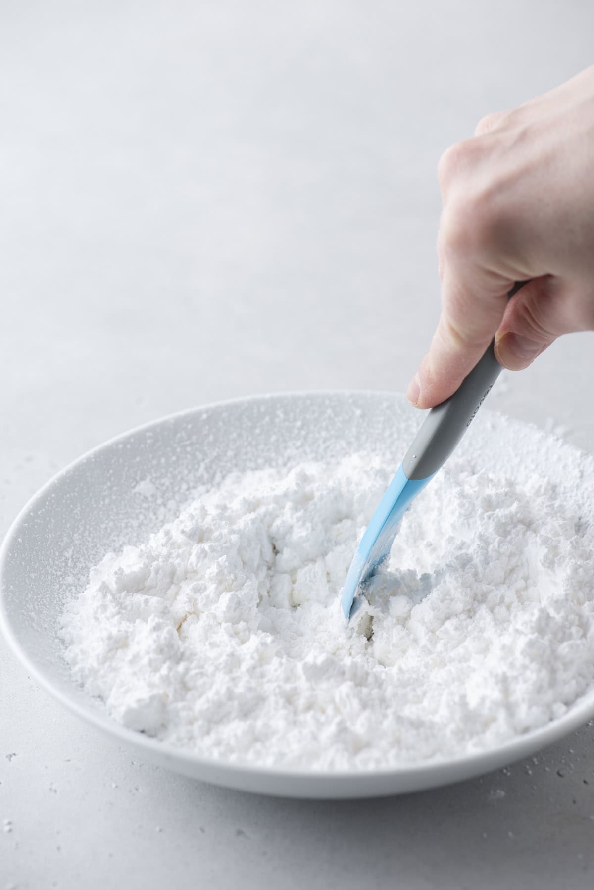 powdered sugar and milk being mixed with a spatula in a white bowl