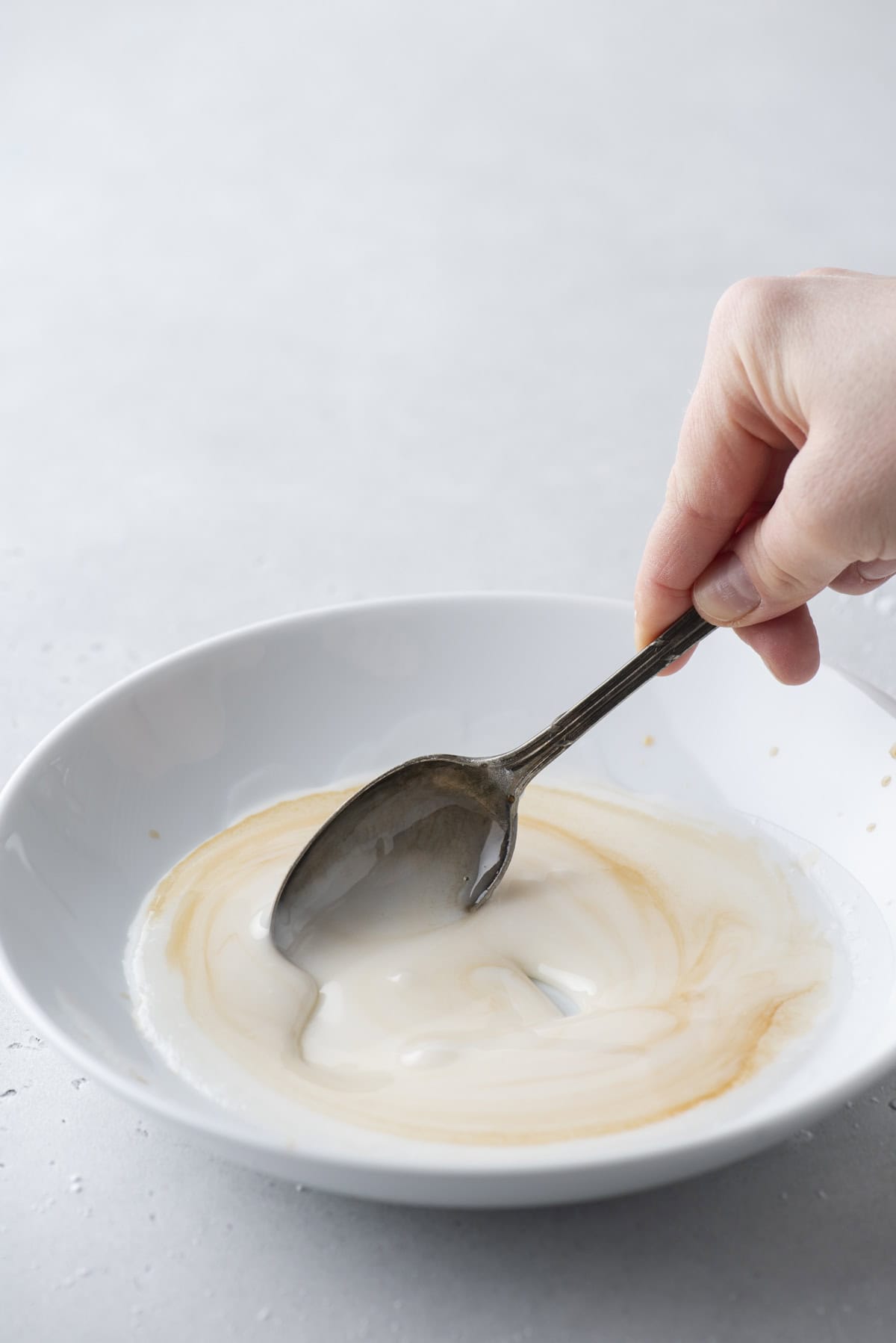 vanilla extract being mixed into a white bowl of donut glaze