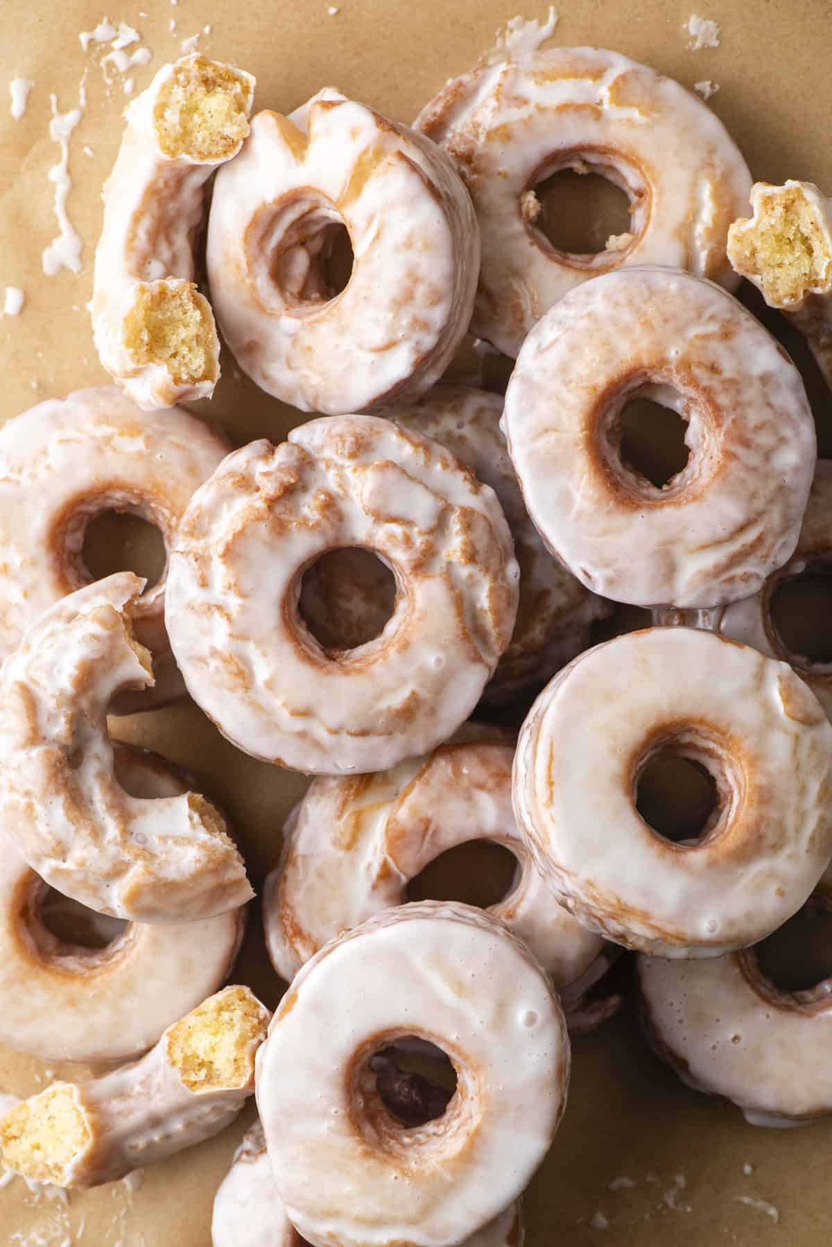 overhead view of glazed donuts stacked and scattered on a brown paper surface