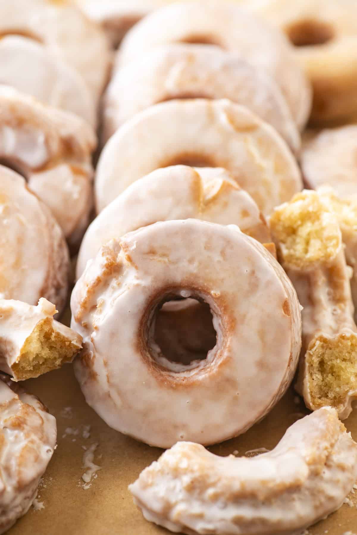 old fashioned donuts covered in donut glaze in rows and scattered around in pieces