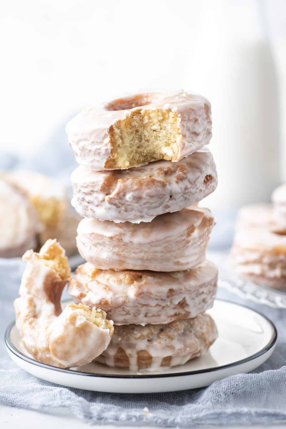 a stack of glazed donuts on a plate with a bite missing out of the top donut and half a donut leaning on the side of the stack