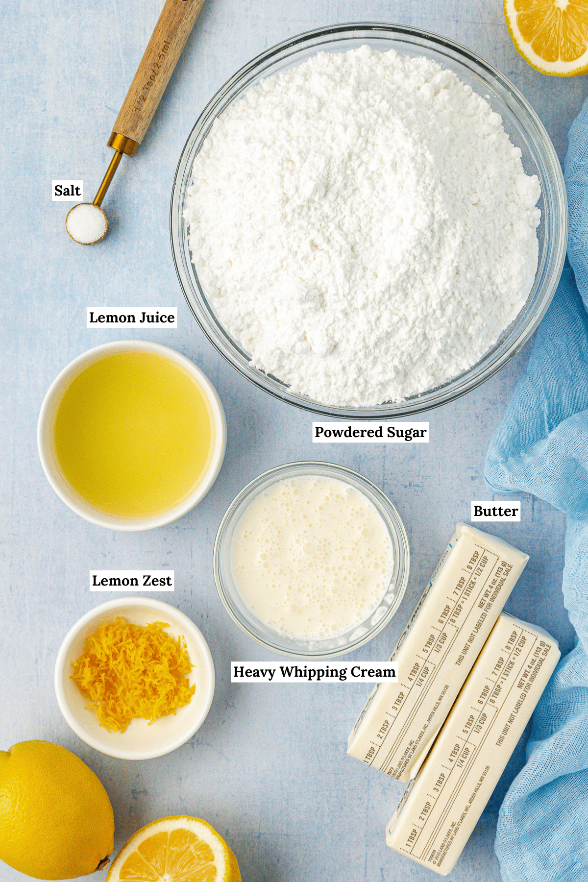 overhead view of the ingredients for lemon frosting including salt, powdered sugar, lemon juice, lemon zest, heavy whipping cream, and butter