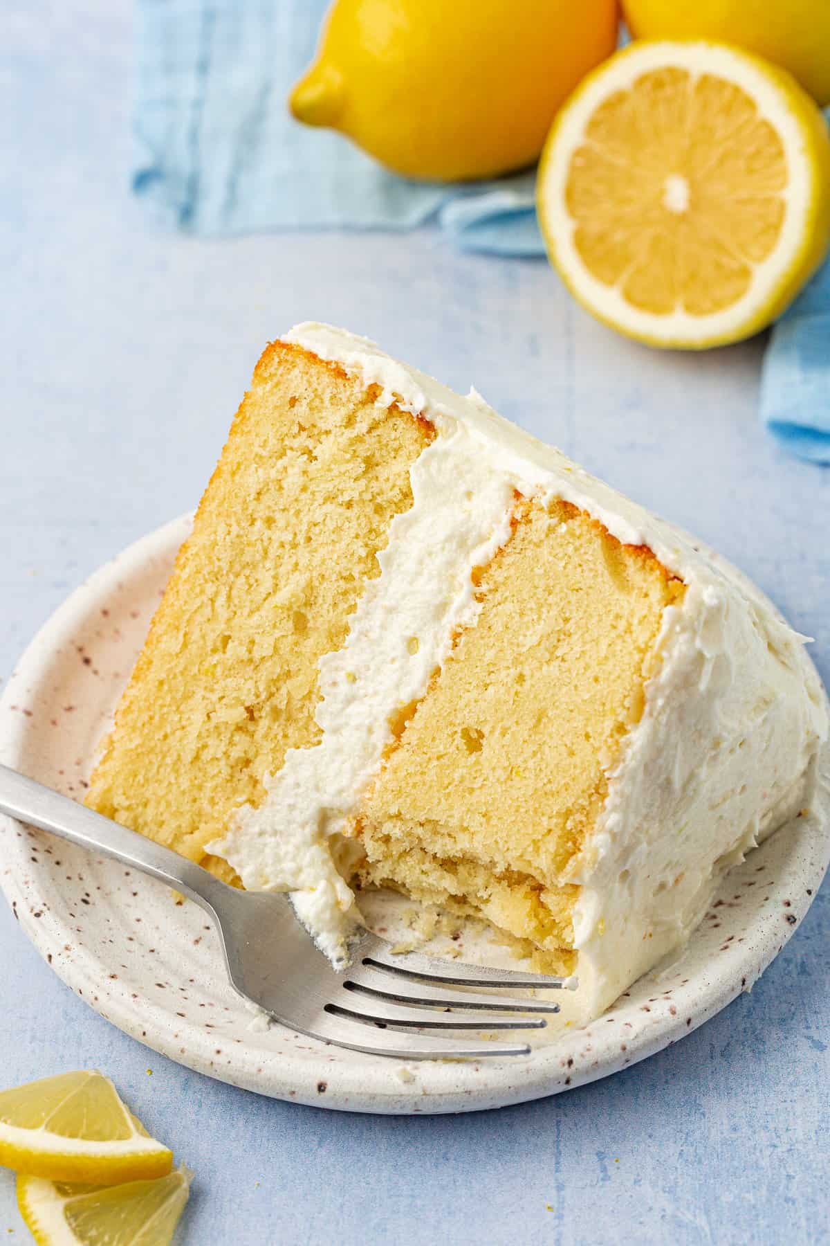 a slice of layer cake on a small plate with a fork, surrounded by fresh lemons