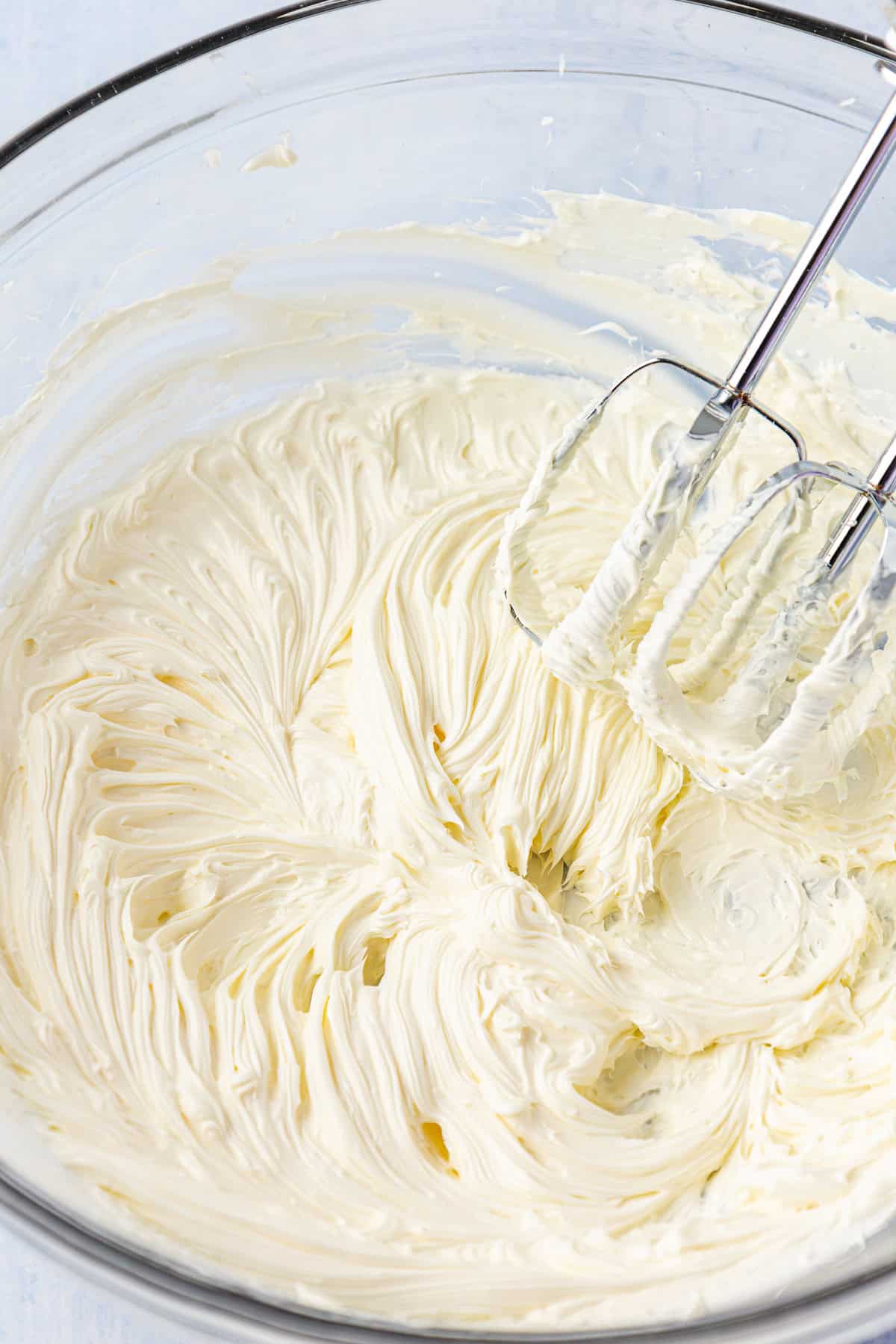 frosting in a clear glass bowl with an electric mixer leaning on the inside