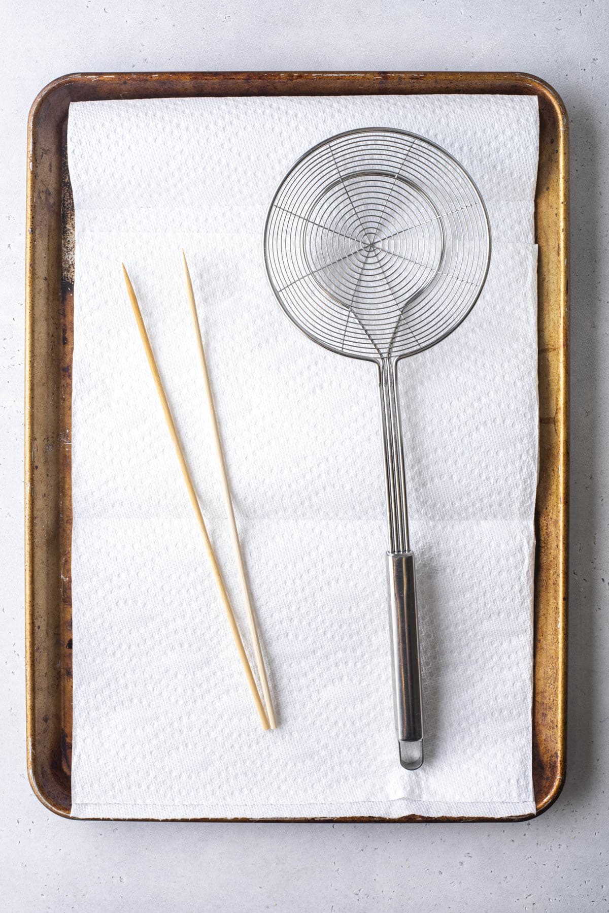 skewers and a spider strainer on a paper towel lined baking sheet