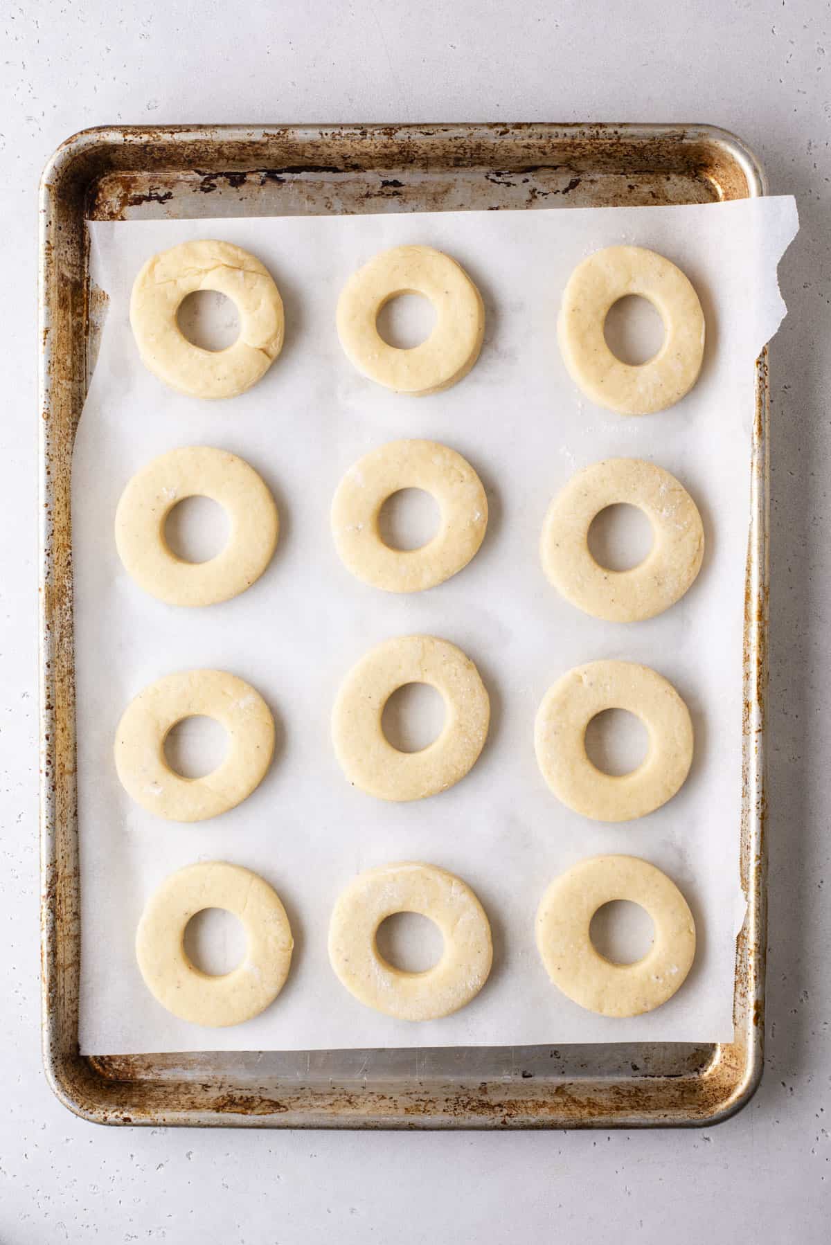 old fashioned donut dough cut into donut shapes and sitting in rows on a baking sheet lined with paper towels