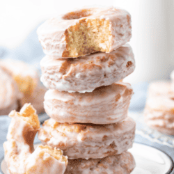 a stack of 5 donuts on a small white place with a bite missing out of the top donut and half a donut leaning on the side of the stack, more donuts on plates in the background