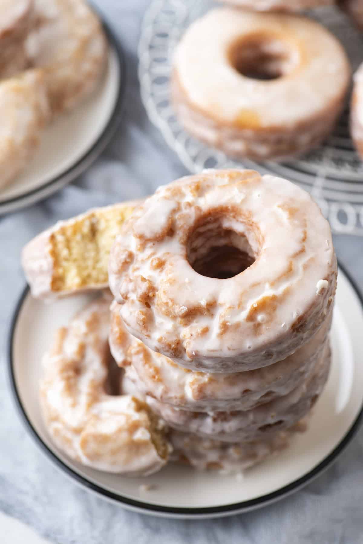 a stack of old fashioned donuts on a small white plate surrounded by more donuts