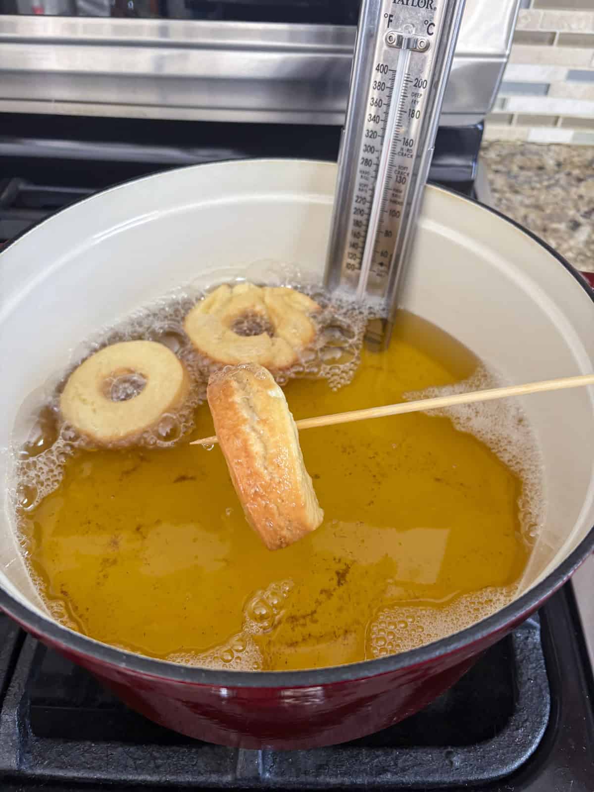 a donut being lifted out of a pot of hot oil with a skewer