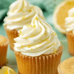 lemon cream cheese frosting on cupcakes topped with lemon zest surrounded by more zest and lemon slices