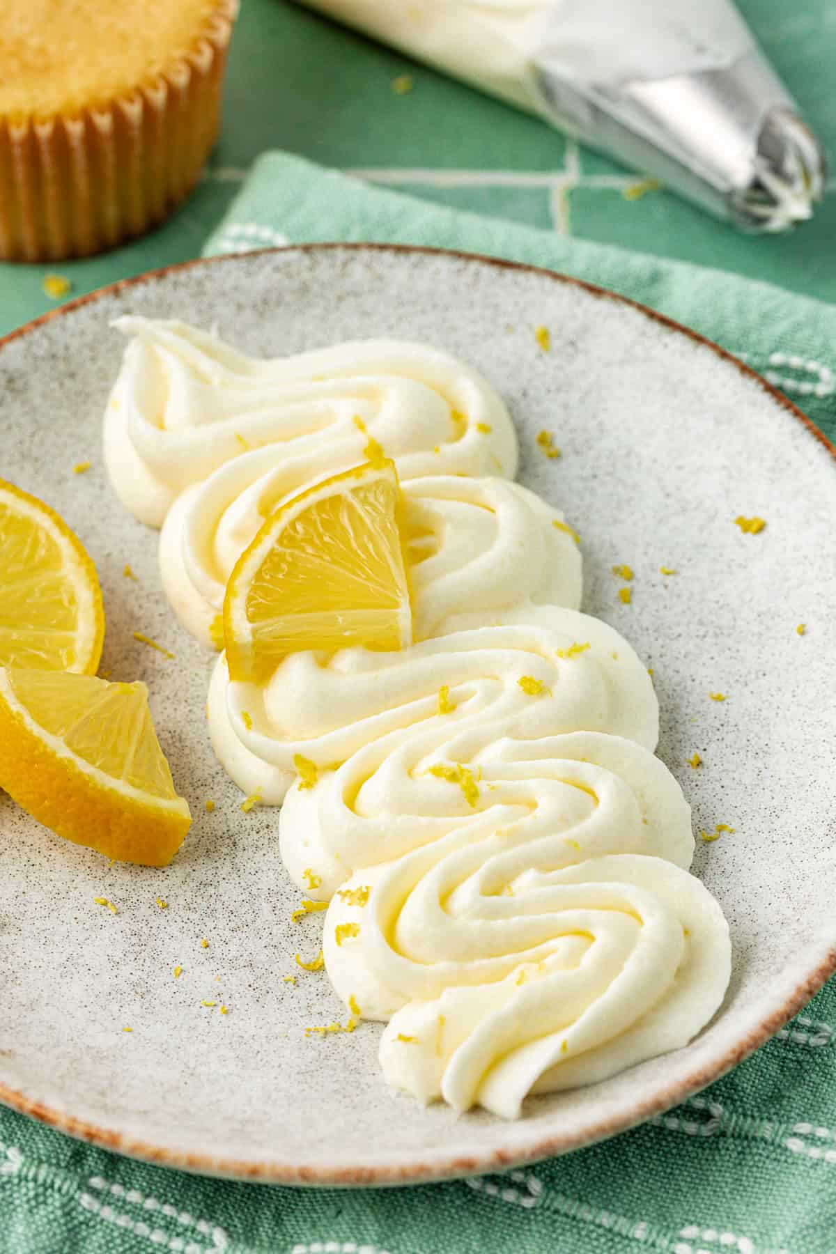 piped lemon cream cheese frosting on a grey plate sprinkled with lemon zest and a lemon wedge and two more lemon wedges on the plate