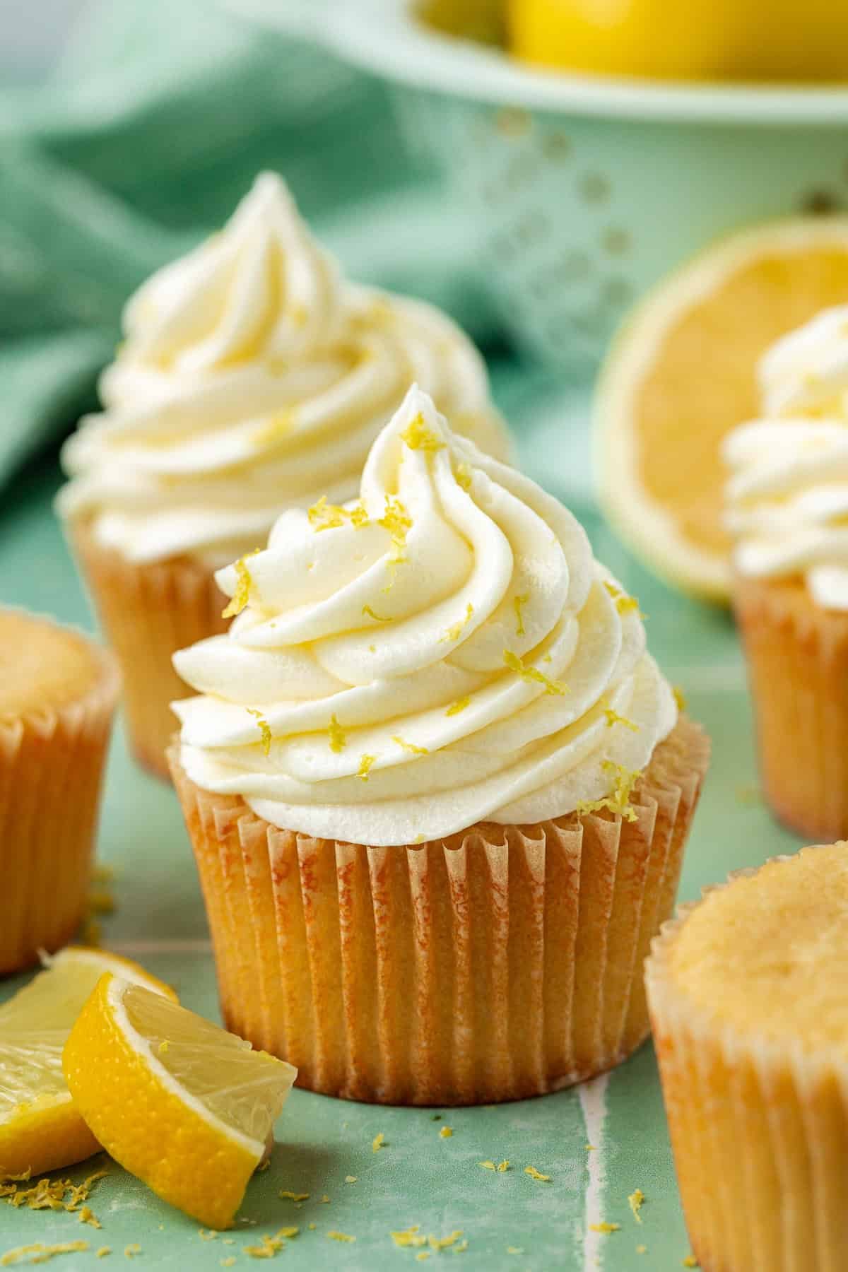 lemon cream cheese frosting on cupcakes topped with lemon zest surrounded by more zest and lemon slices