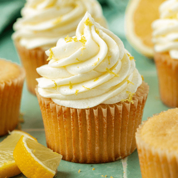 lemon cream cheese frosting on cupcakes topped with lemon zest surrounded by more zest and lemon slices