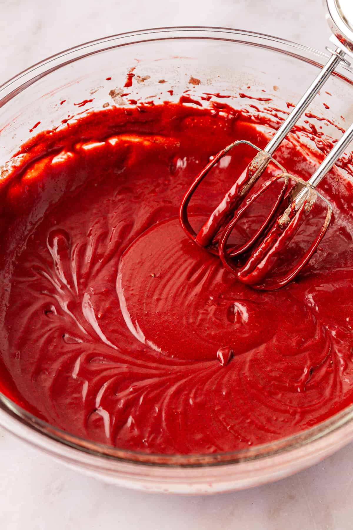 brownie batter in a clear glass mixing bowl with an electric mixer leaning on the side