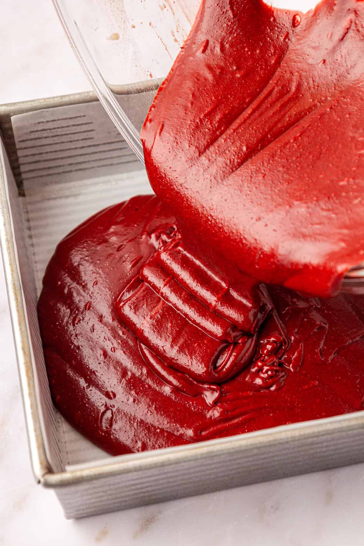 batter being poured out of a clear glass bowl into a square baking pan