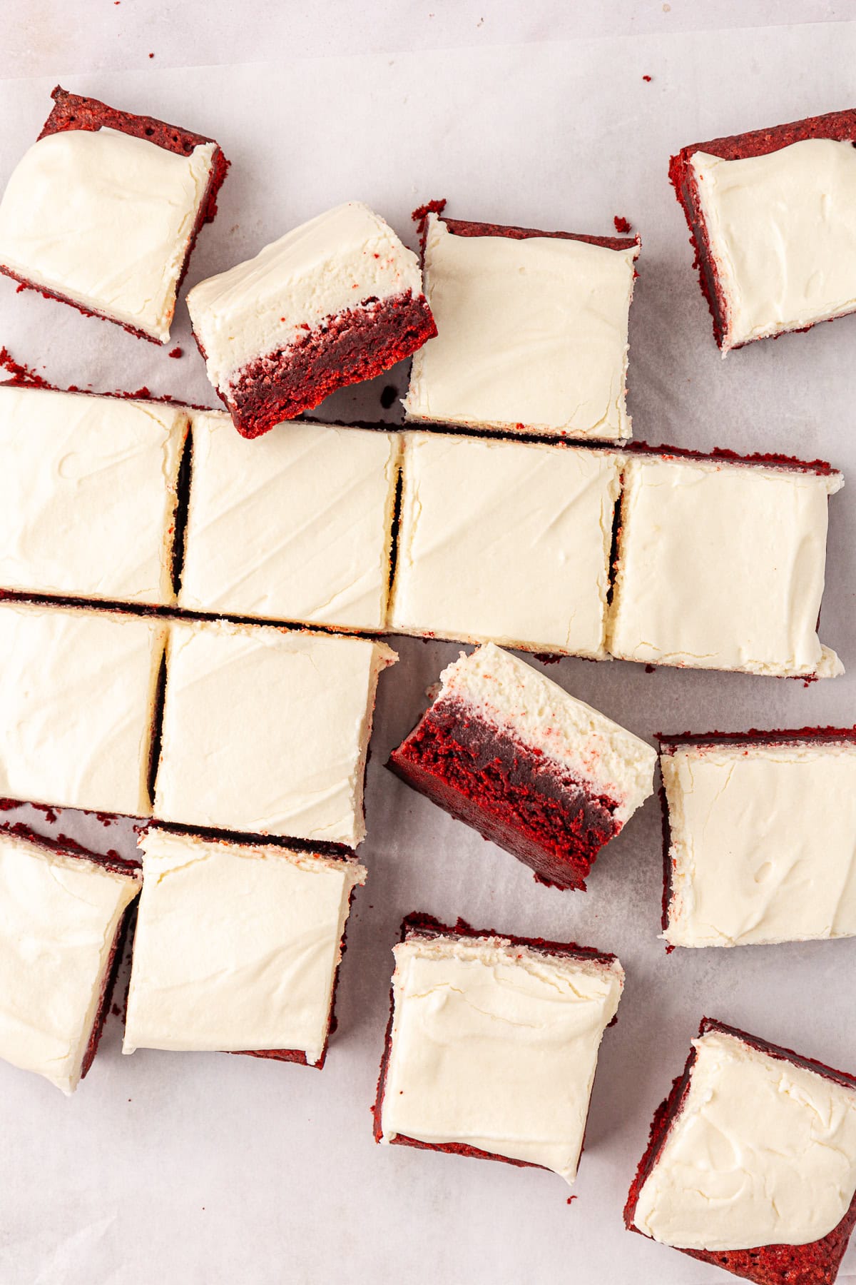 overhead view of scattered red velvet brownies topped with cream cheese frosting, some in rows, some leaning on others and some on their sides showing the two layers of brownie and frosting