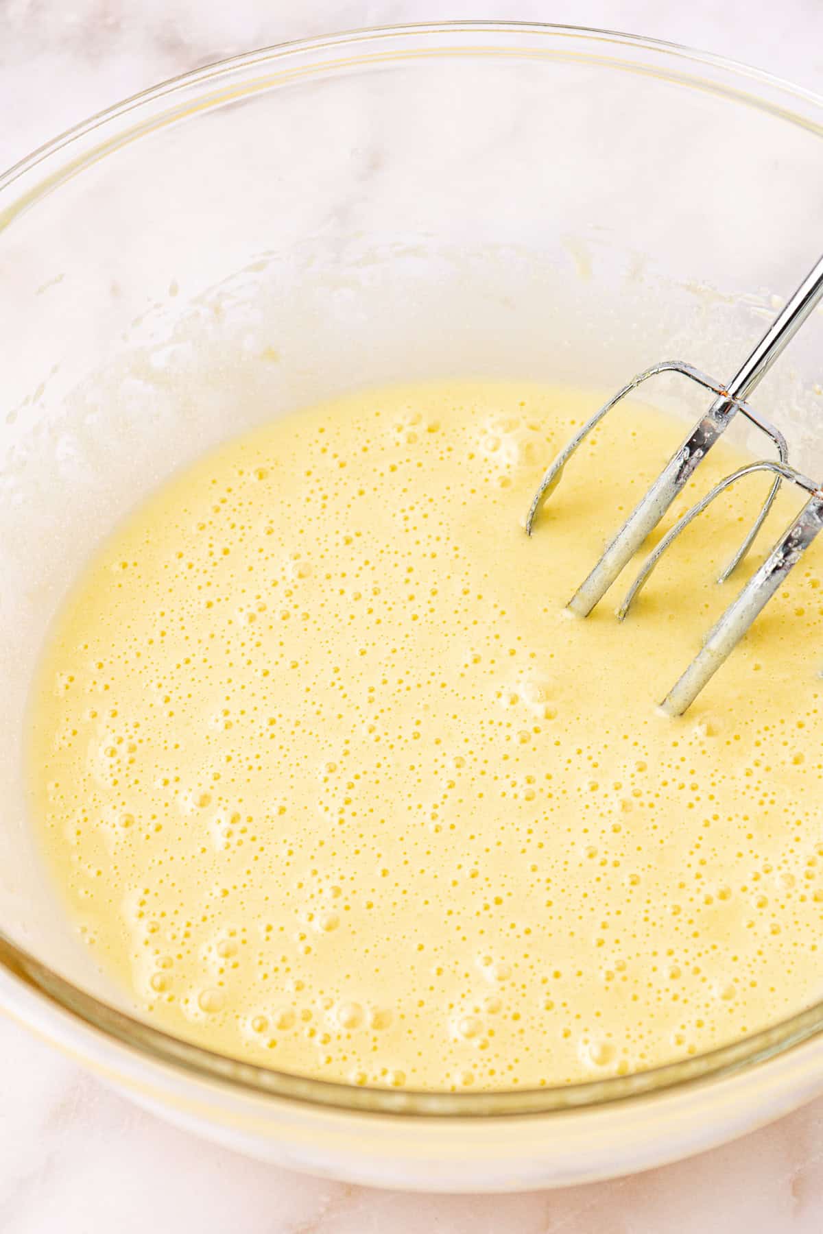 wet ingredients for red velvet brownies in a clear glass bowl with electric mixers leaning on the inside of the bowl