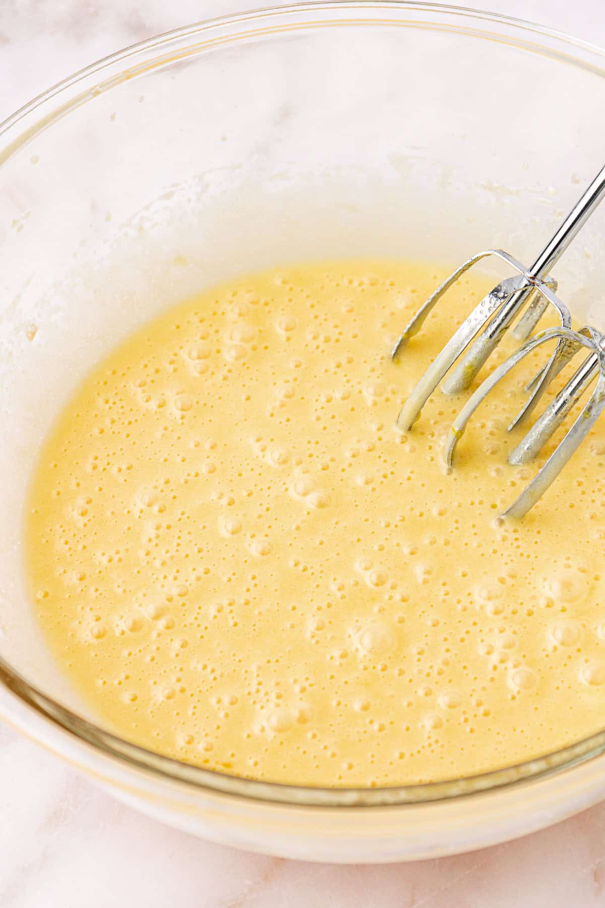 wet ingredients for red velvet brownies in a clear glass bowl with electric mixers leaning on the inside of the bowl