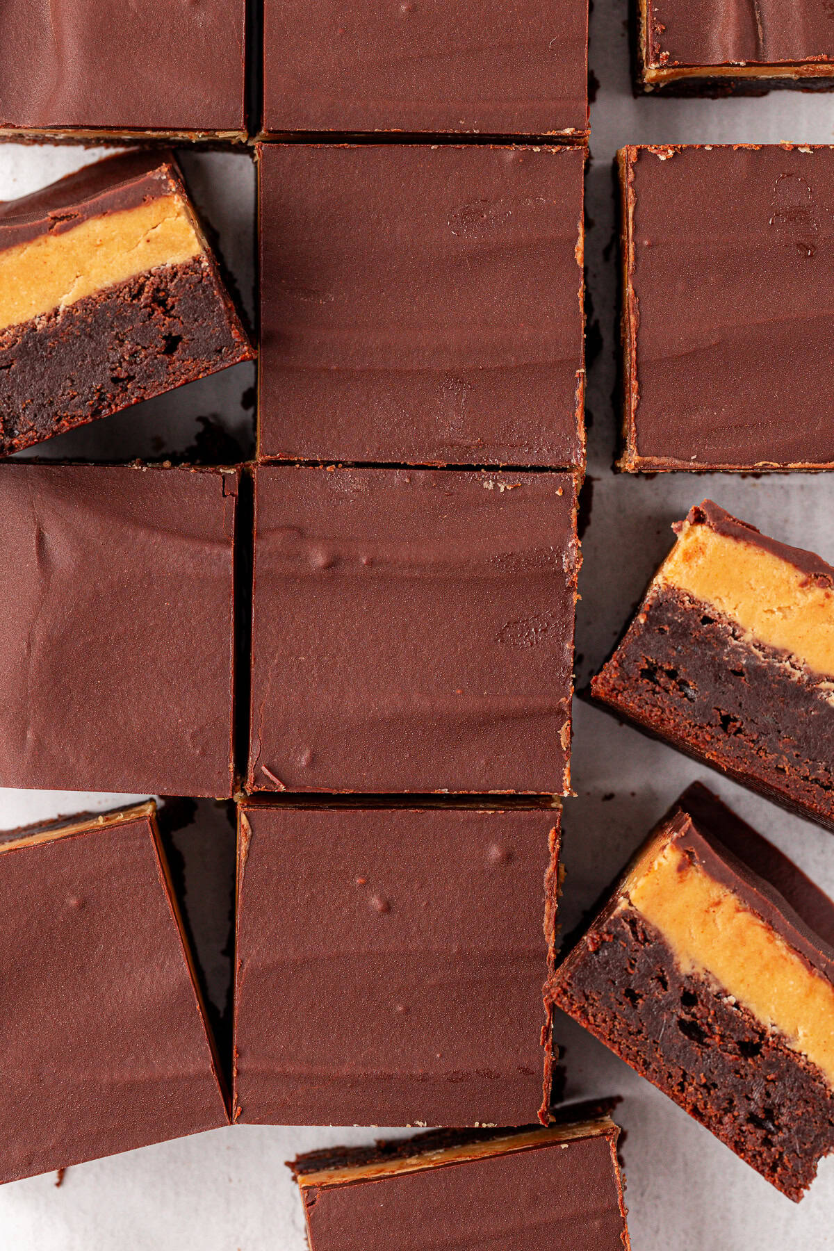 Buckeye brownies with three layers: a thick, glossy chocolate top, a peanut butter middle, and a dark brownie base. Some bars are stacked to show the distinct layers and rich textures.